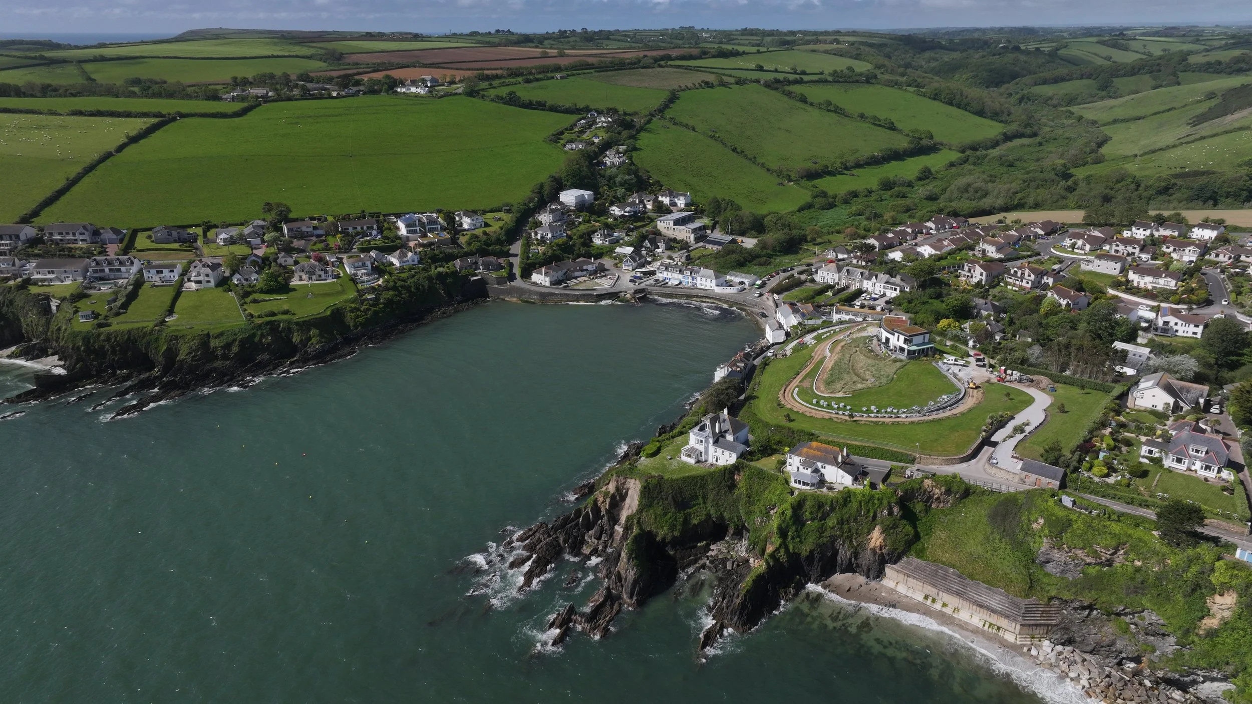 Aerial view of a coastal town with houses, greenery, and a large body of water along the rocky shoreline.