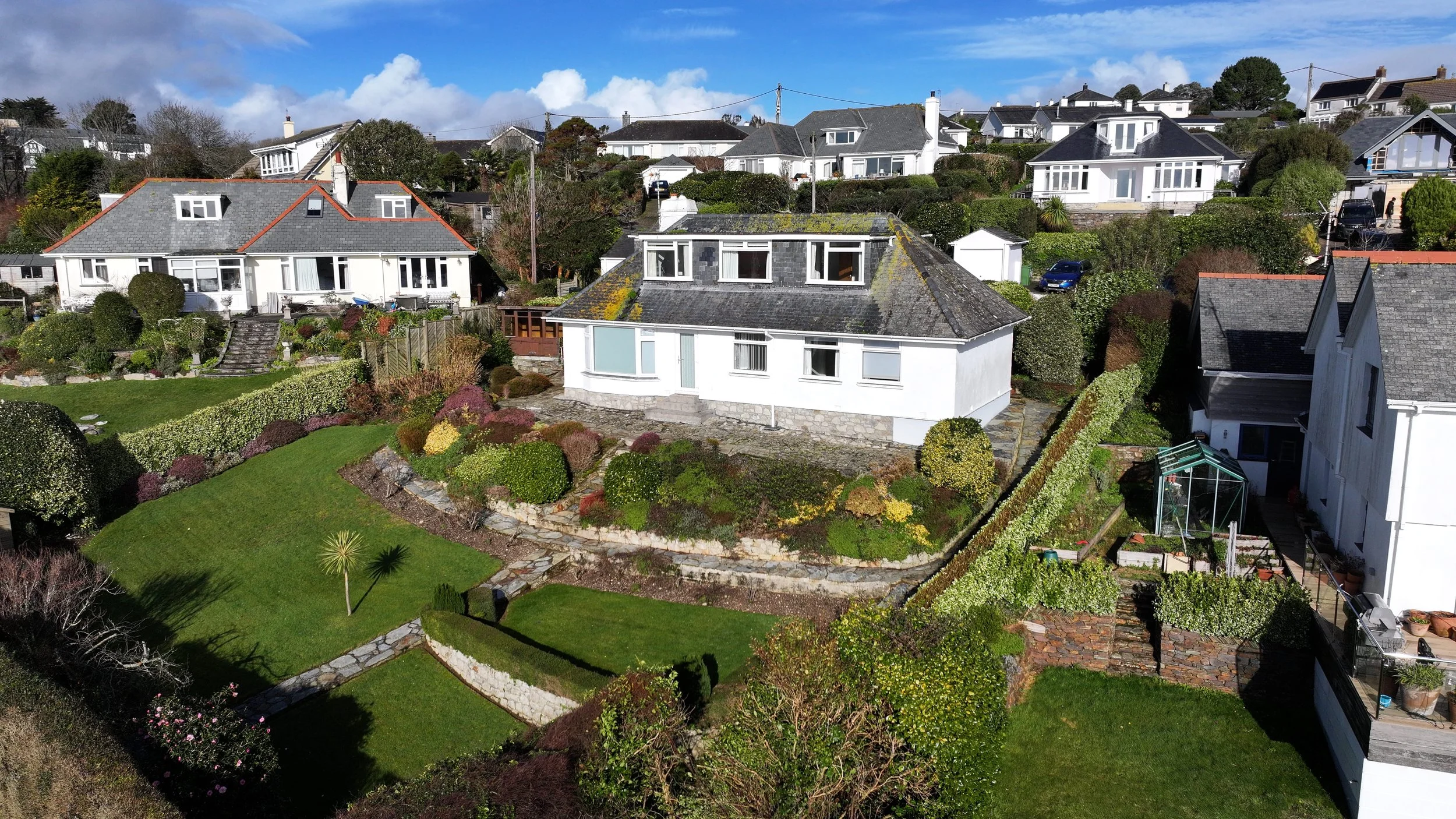 Aerial view of a neighborhood with white houses, green lawns, and a clear blue sky with some clouds.
