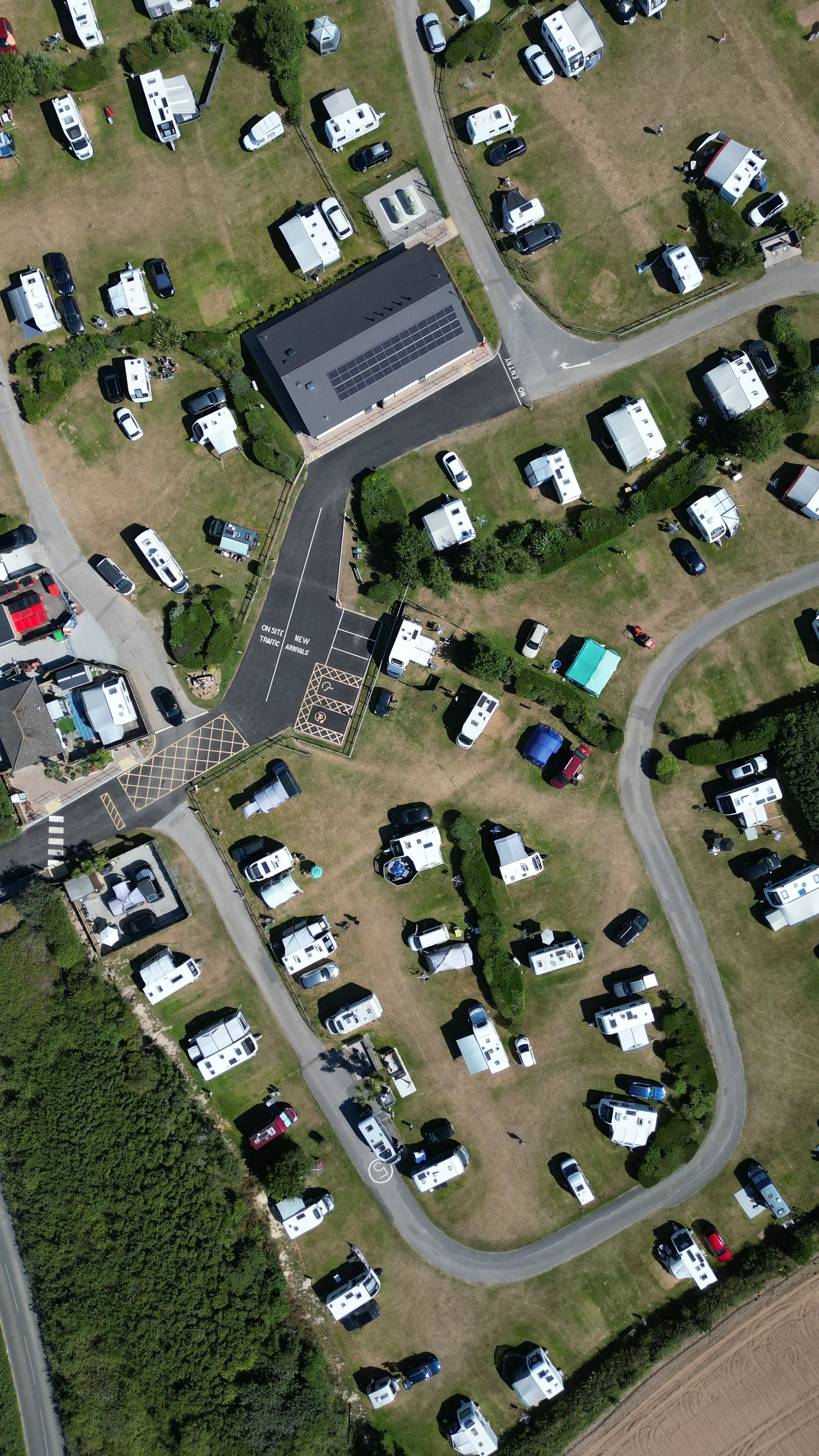 Aerial view of a campsite with numerous RVs, trailers, and tents on grassy areas, with winding roads and trees surrounding the site.