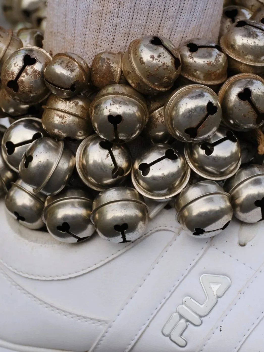 Close-up of multiple silver metallic bells with heart-shaped cutouts, placed on a white sneaker.