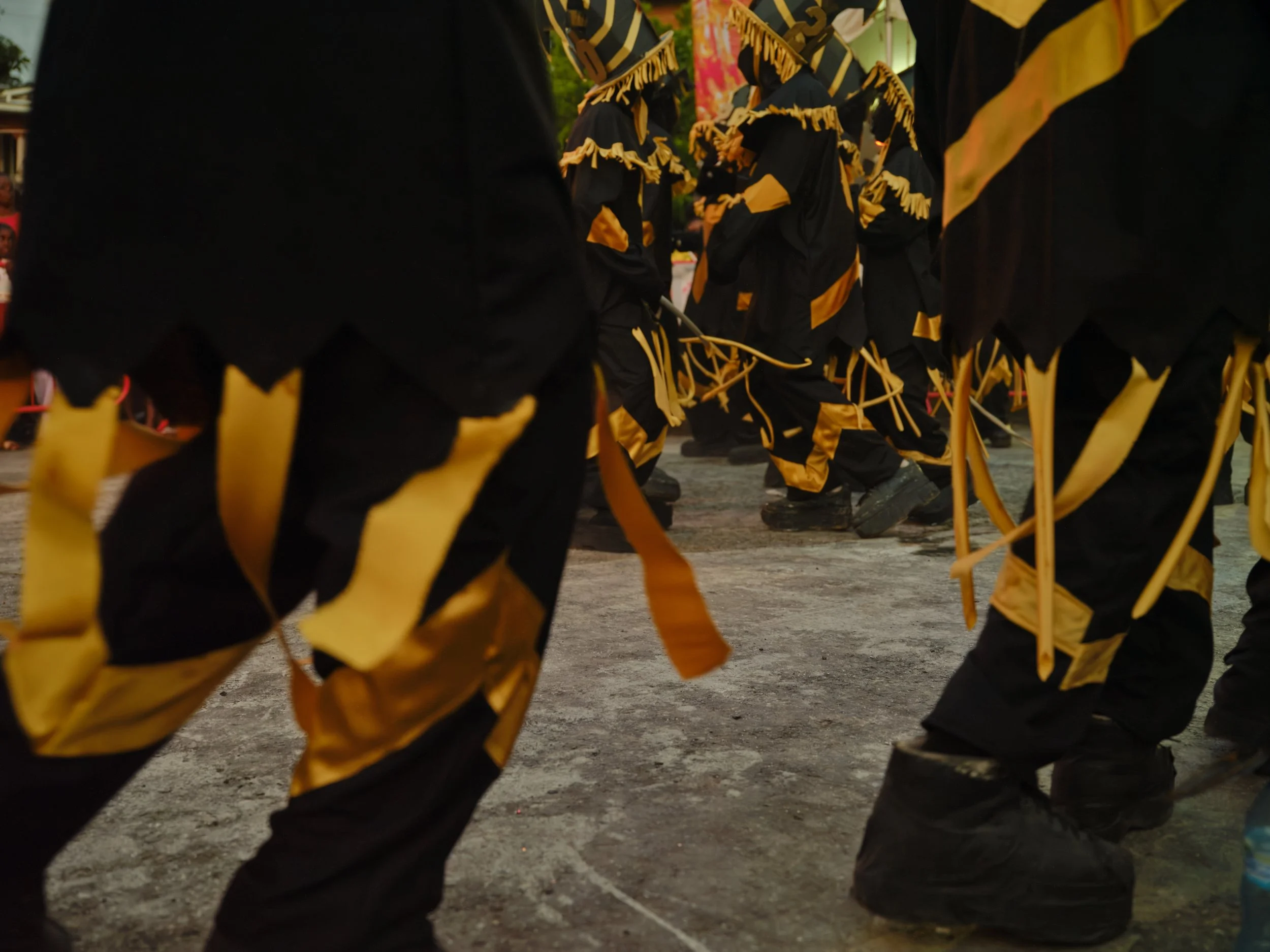 Group of musicians in black with gold accents playing traditional instruments at an outdoor event.