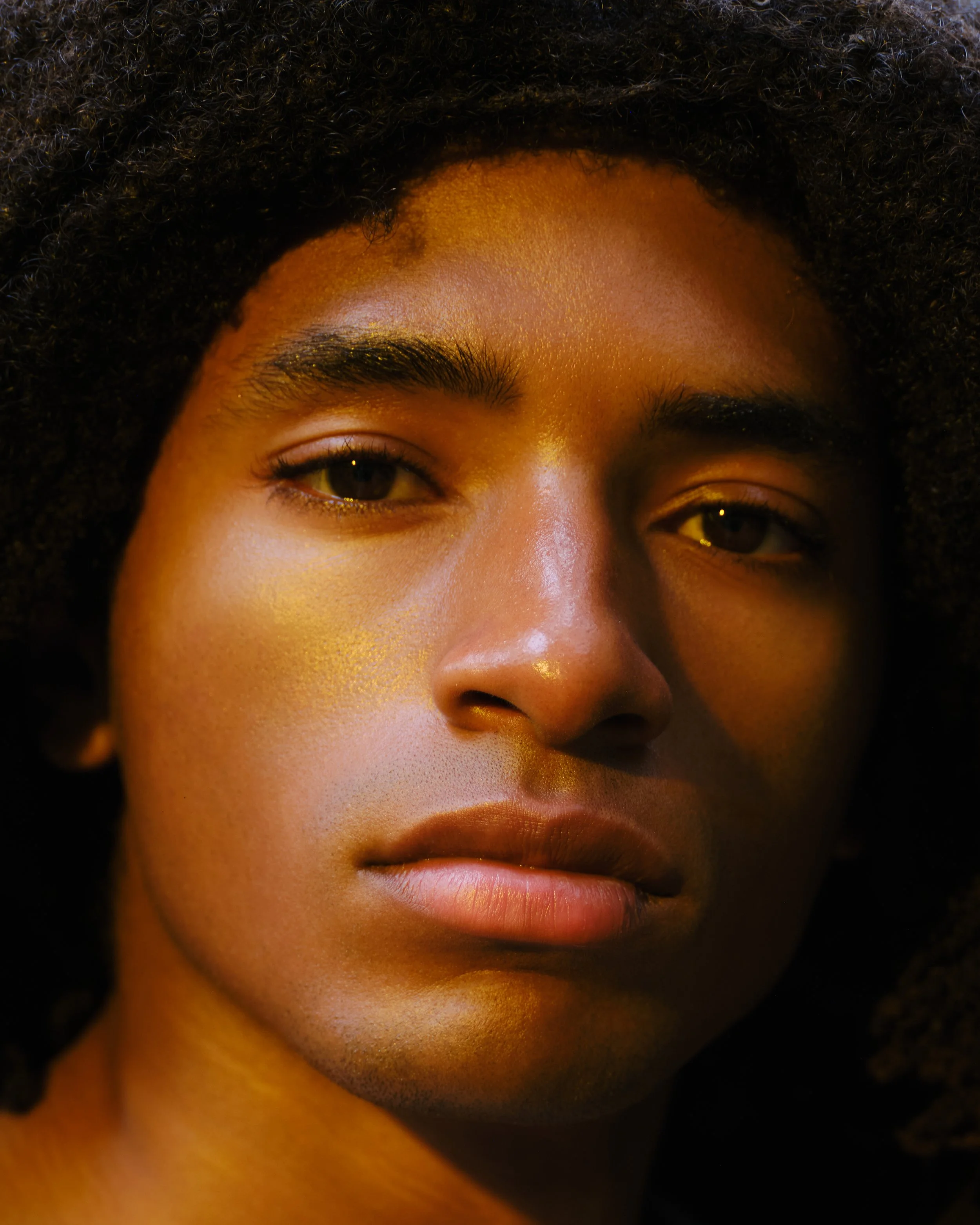 Close-up of a person's face, showing from the eyebrows to the lips, with curly hair and smooth skin.