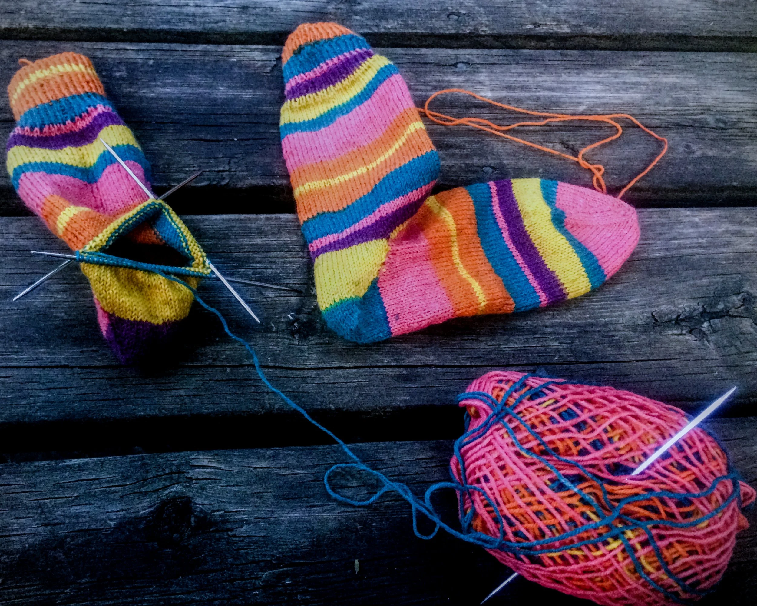A pair of half finished knitted striped socks, complete with knitting needles.