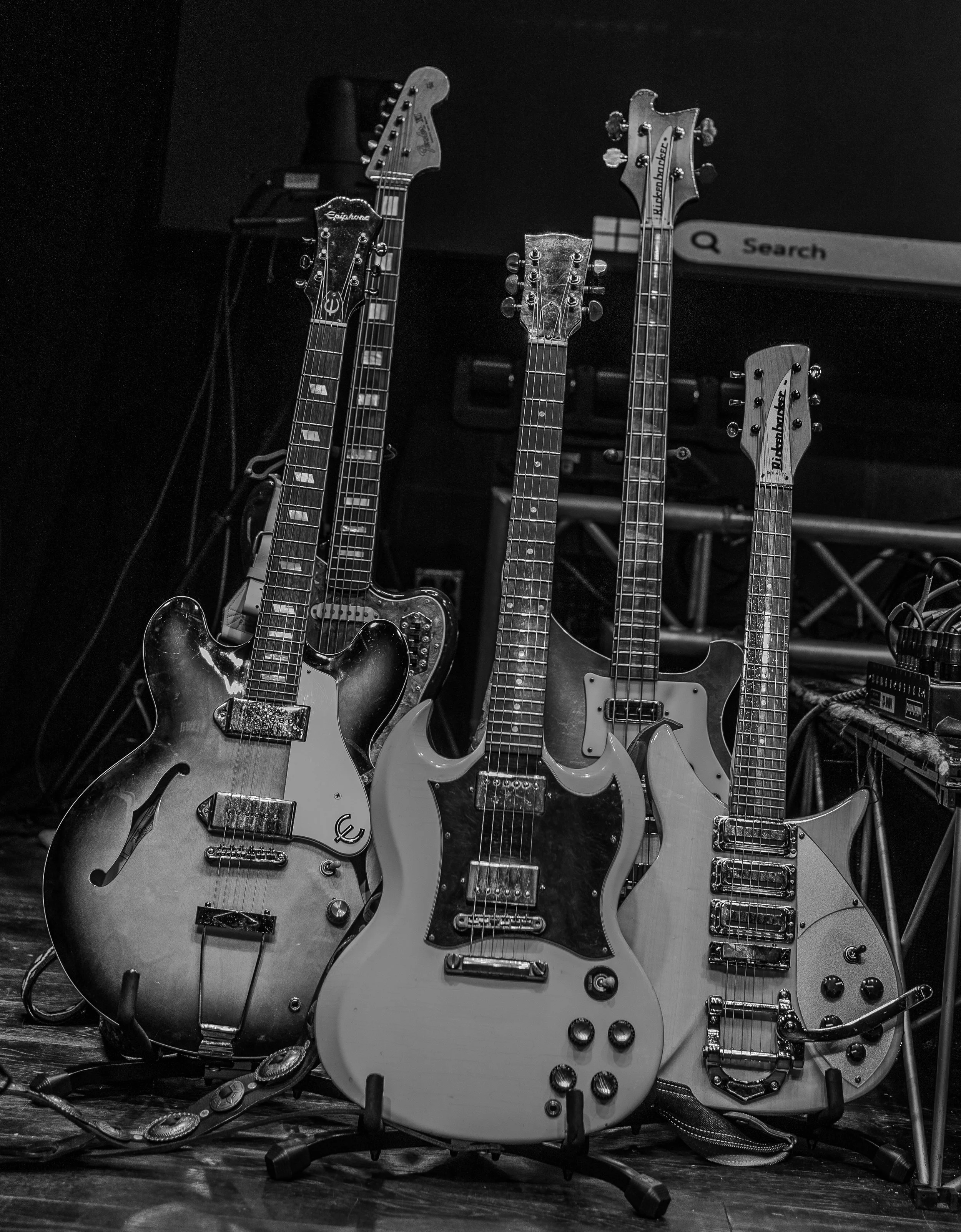 Black and white photo of five electric guitars standing upright on a stage.
