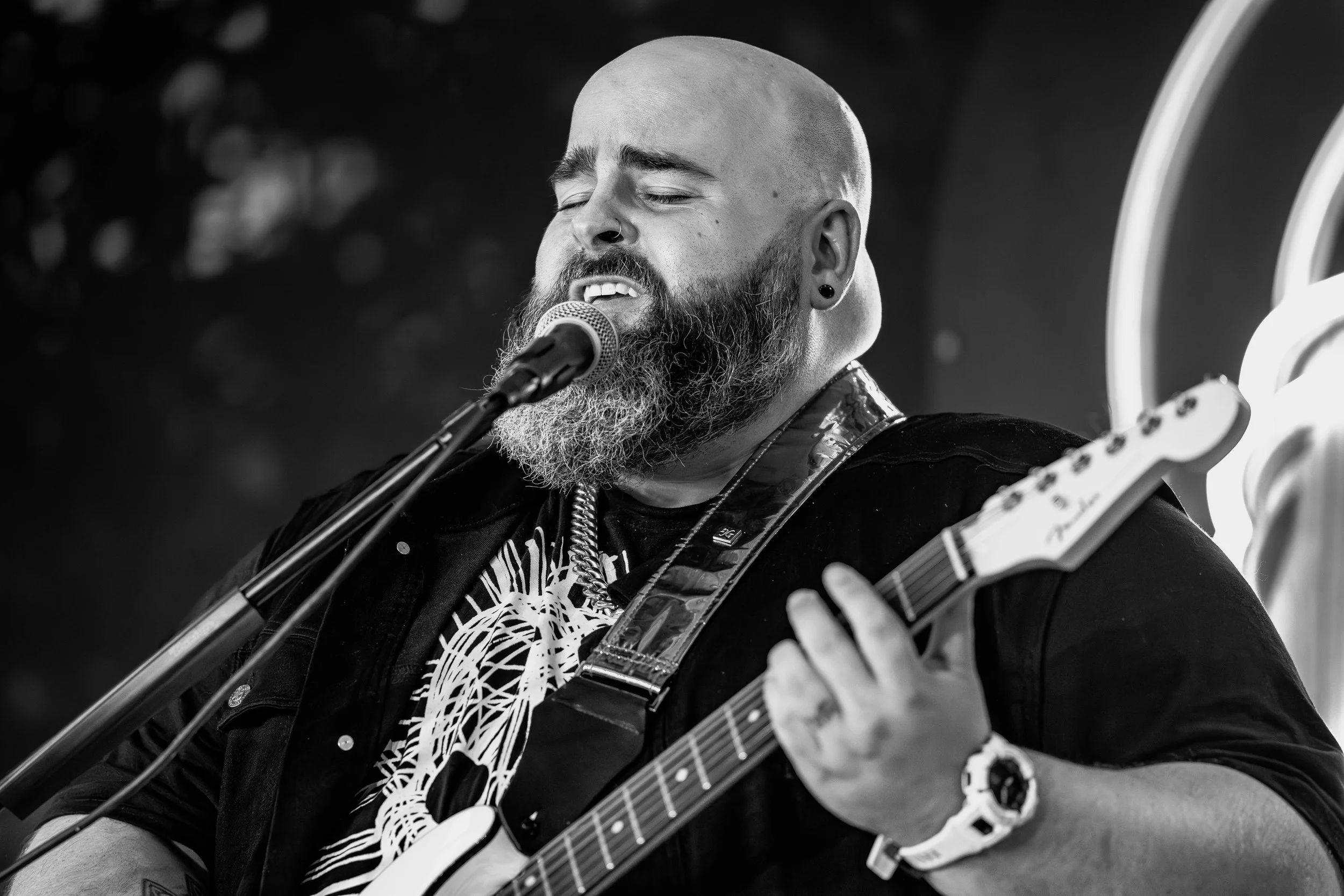 Black and white photo of a bearded musician singing and playing an electric guitar with eyes closed.
