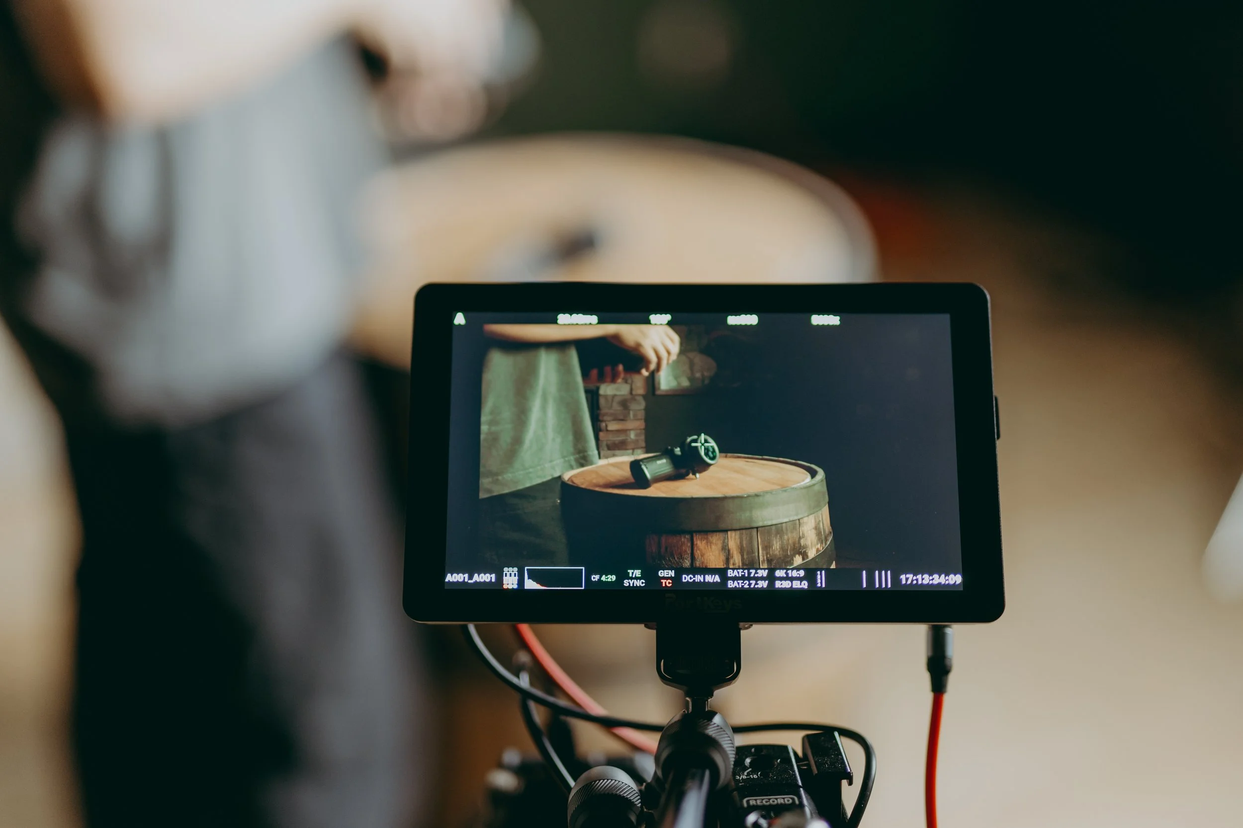 Video camera monitor capturing a person in a green shirt filming a black object on a wooden barrel.