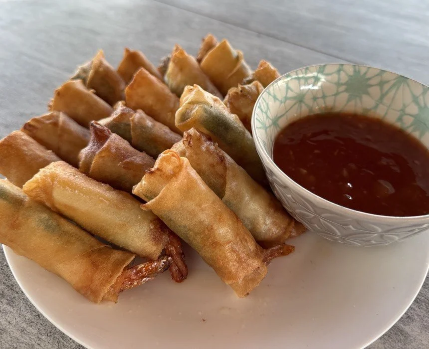 A plate of crispy fried spring rolls with a bowl of dipping sauce on the side.