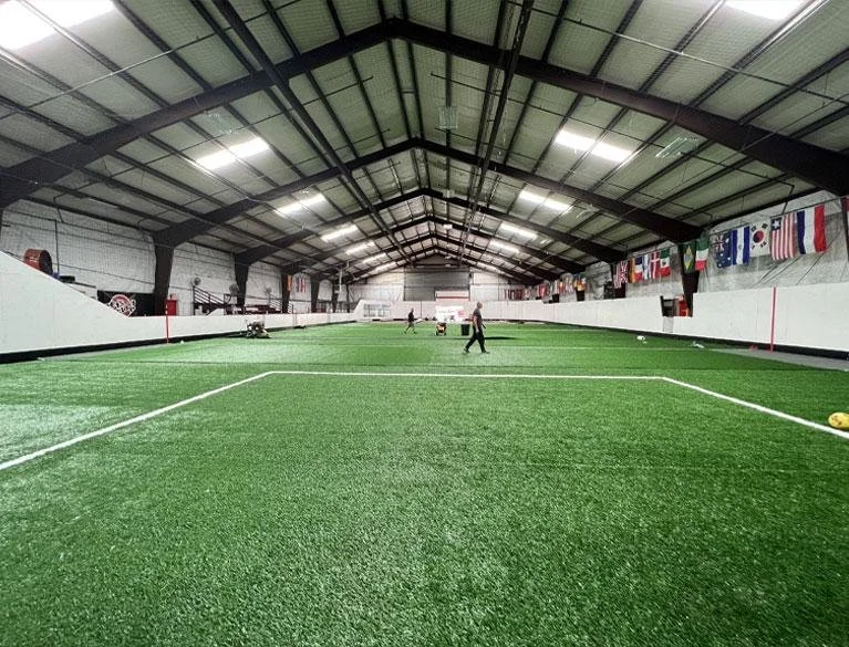 Indoor soccer field with artificial turf, players, and international flags displayed along the walls.