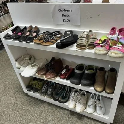 Display shelf of children's shoes priced at $2.00, including various styles of sneakers, sandals, boots, and dress shoes.
