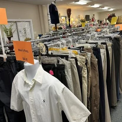 Clothing racks with men's pants and a white shirt on a mannequin in a retail store, with orange price signs.