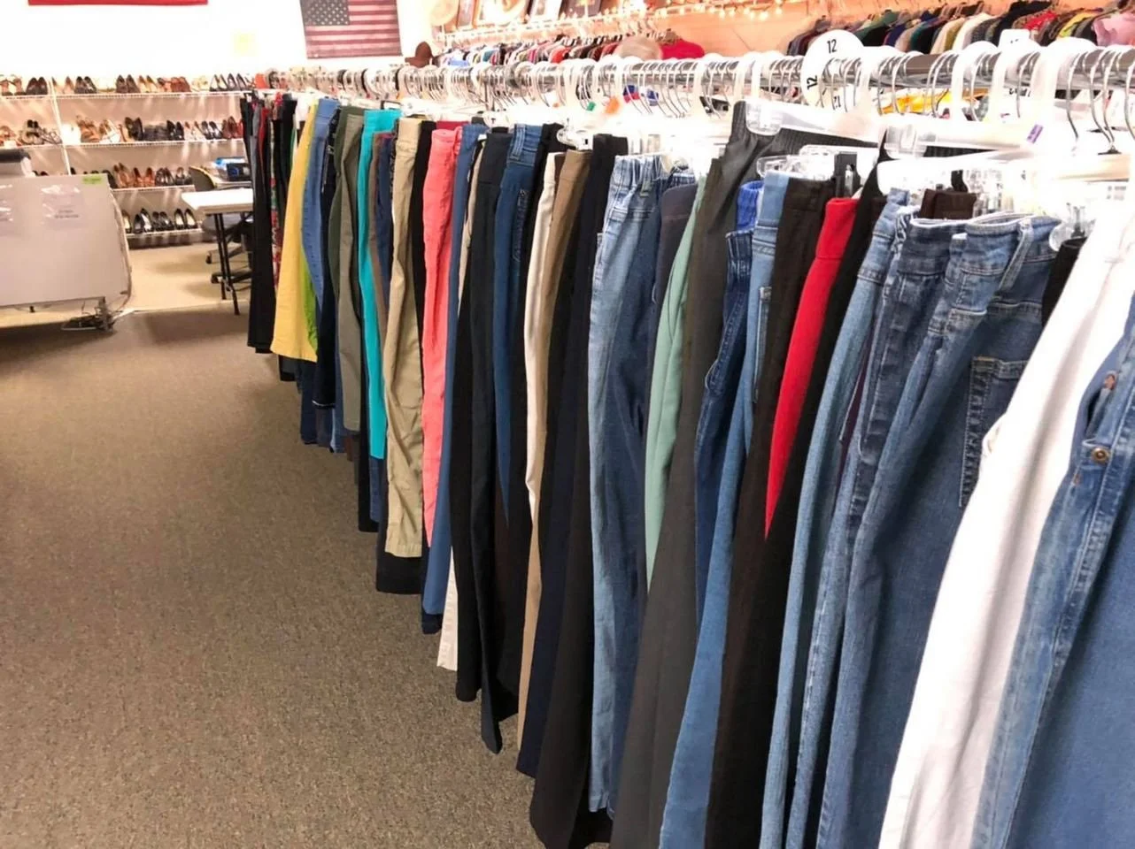 Clothing store with jeans and pants hanging on racks, shelves with shoes in the background, and American flags on the wall.