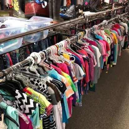 Clothing rack with colorful kids' shirts hanging on plastic hangers in a thrift store.