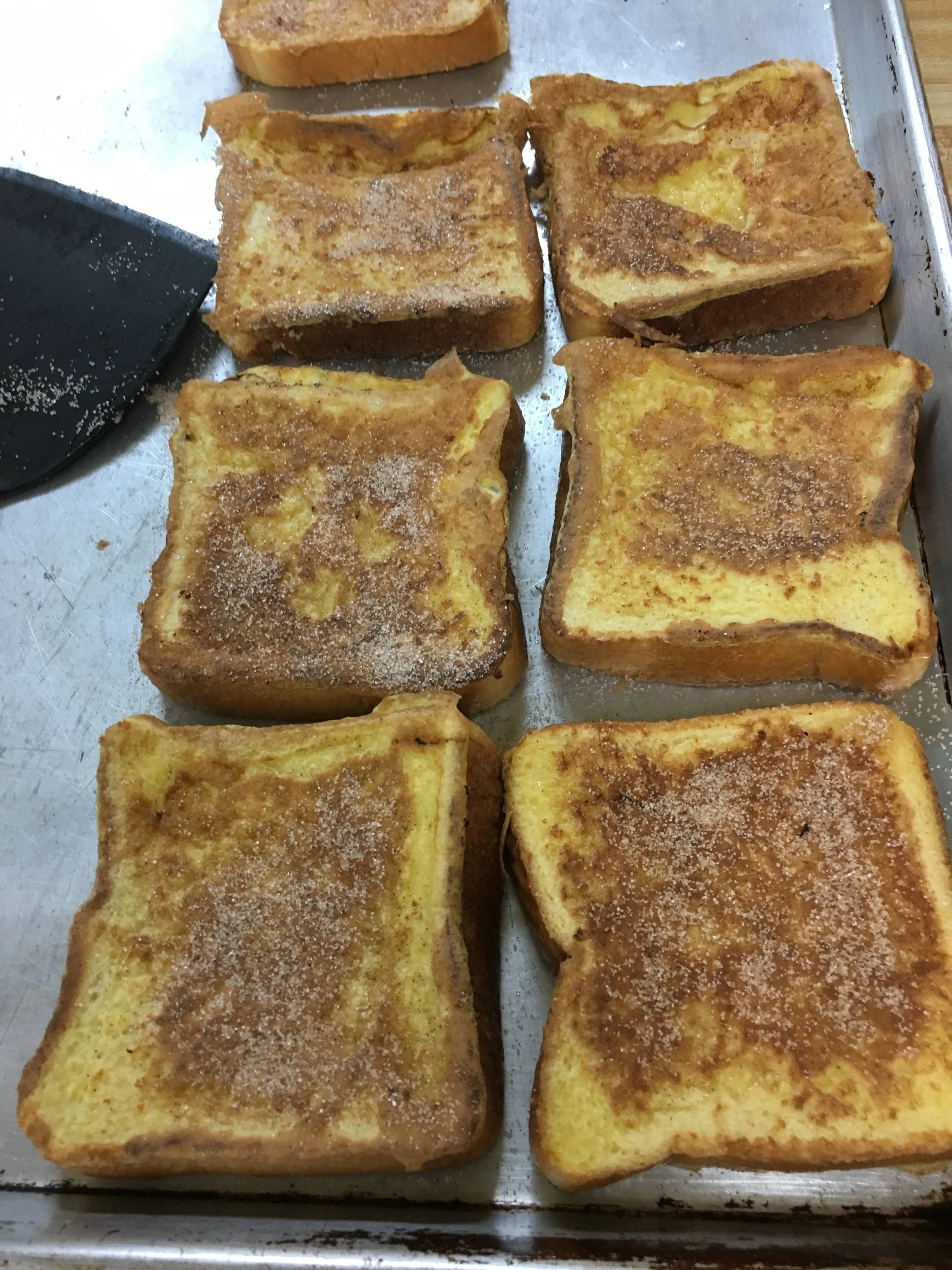 Six slices of French toast with cinnamon and sugar on a baking sheet.