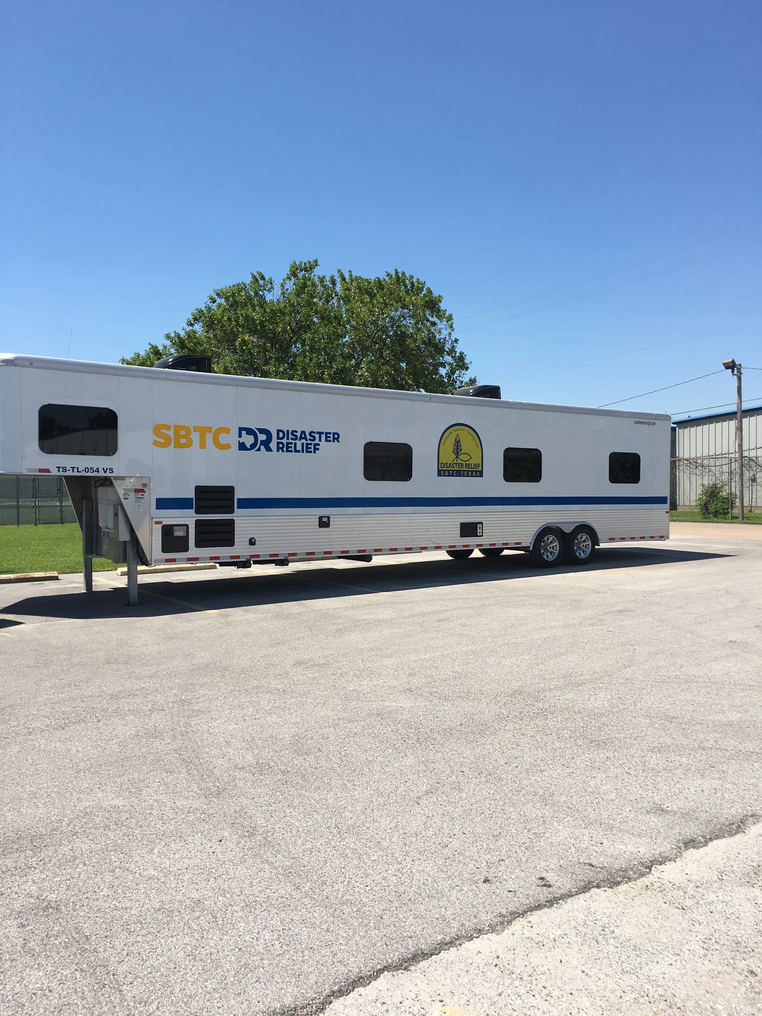 A large mobile disaster relief trailer with 'SBTC Disaster Relief' and related logos, parked on an empty lot under a clear blue sky.