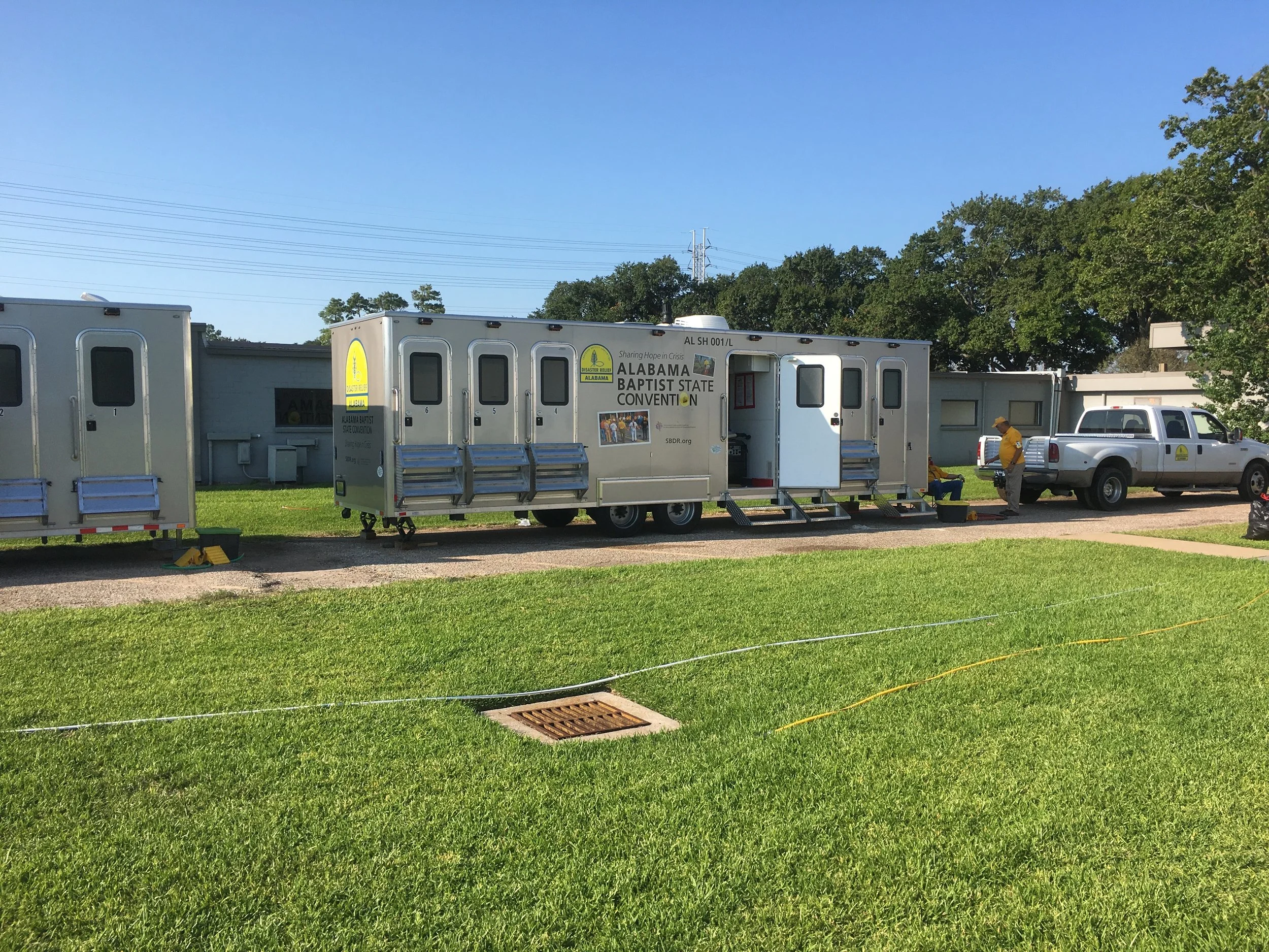Mobile units for Alabama Baptist State Convention on a grassy area with two people in yellow shirts, one sitting, and one standing near a pickup truck.