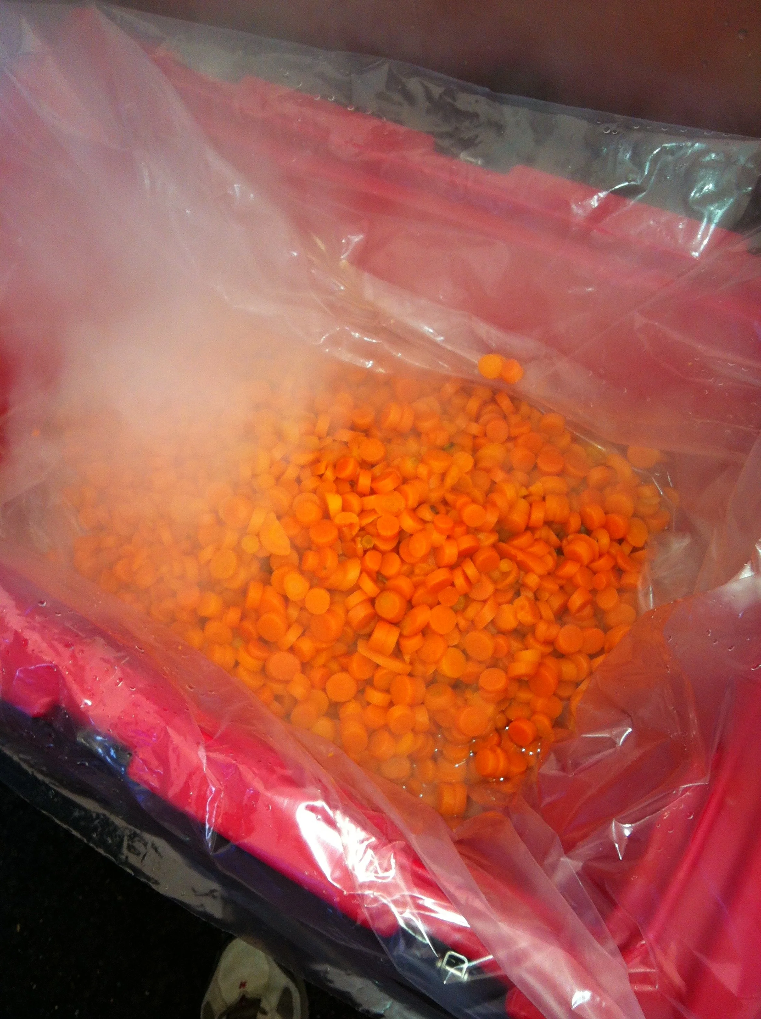 Orange carrots chopped into small rounds inside a plastic bag, with steam rising.