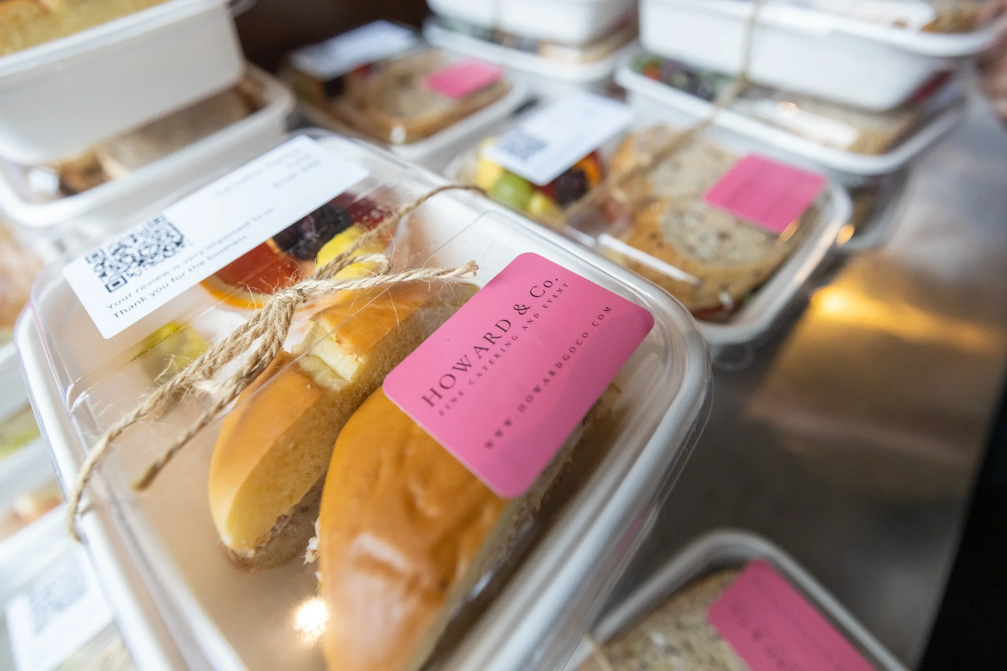 Assorted sandwich lunch boxes with ham, cheese, and lettuce, accompanied by fruit slices and pickles.