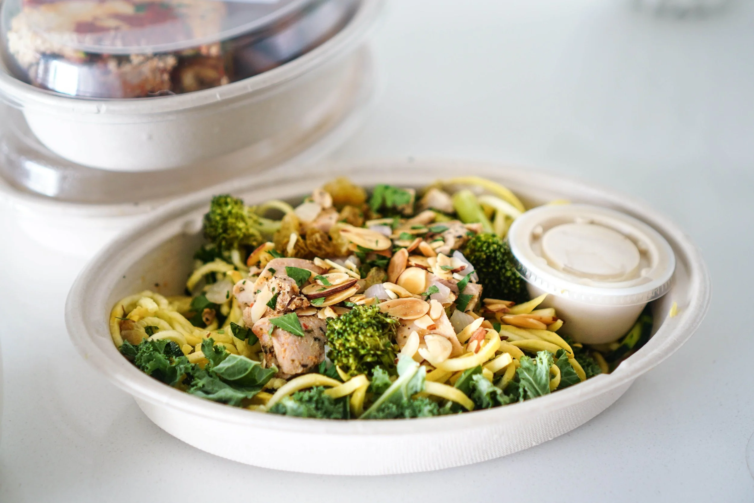 Prepared meals in containers with chicken, mashed potatoes, asparagus, and sauce cups.