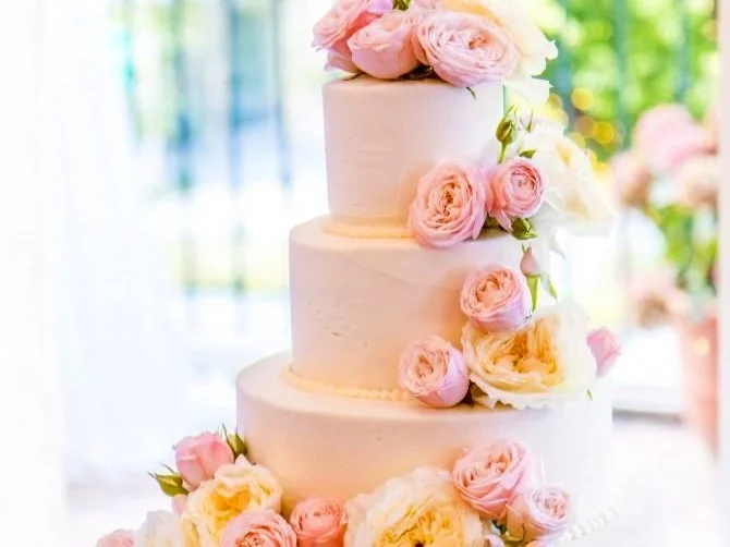 Three-tier white wedding cake adorned with pink and white roses.