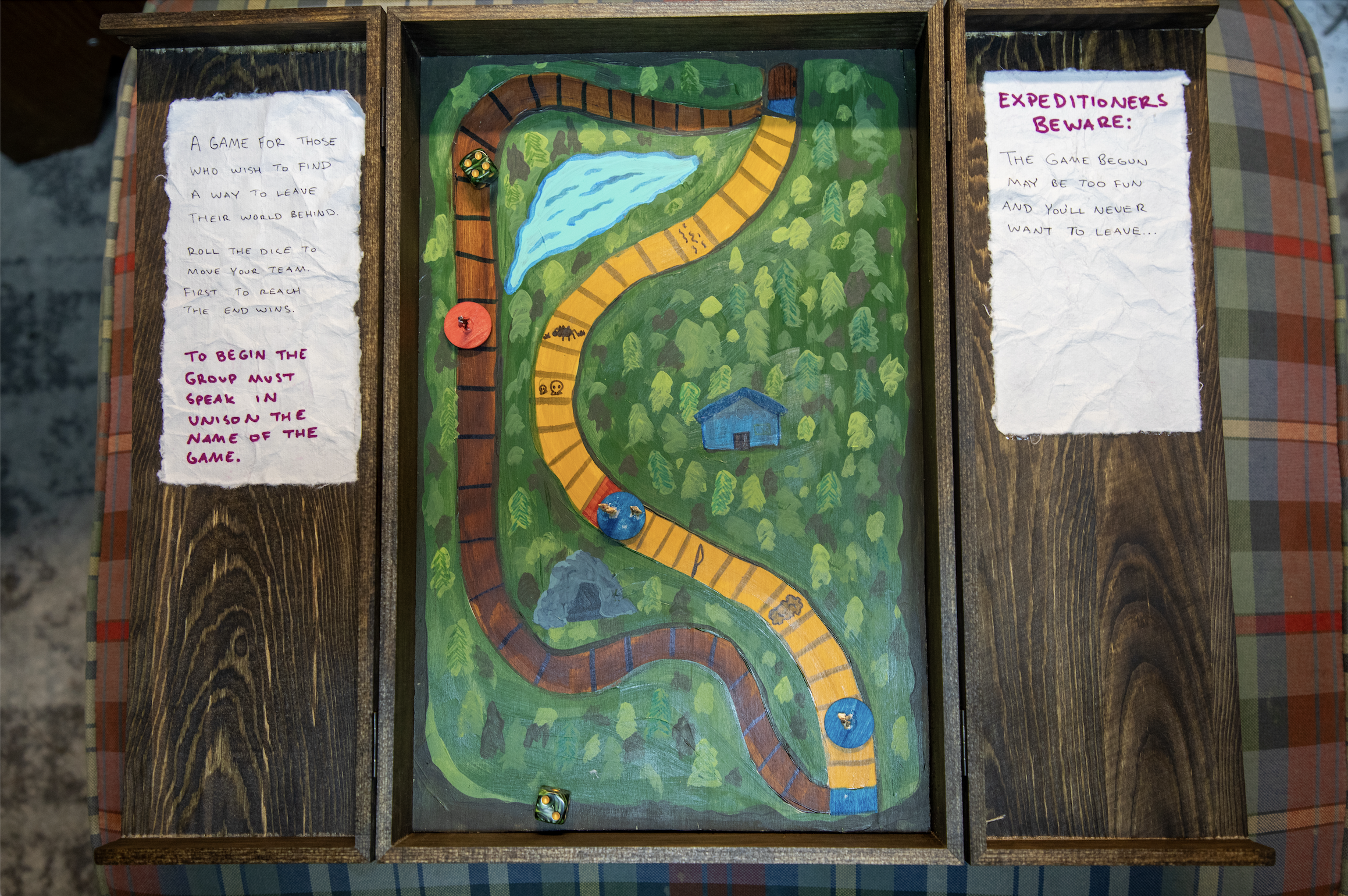 A painted wooden game board with a winding path, water feature, and small house. Its instructions are on either side.