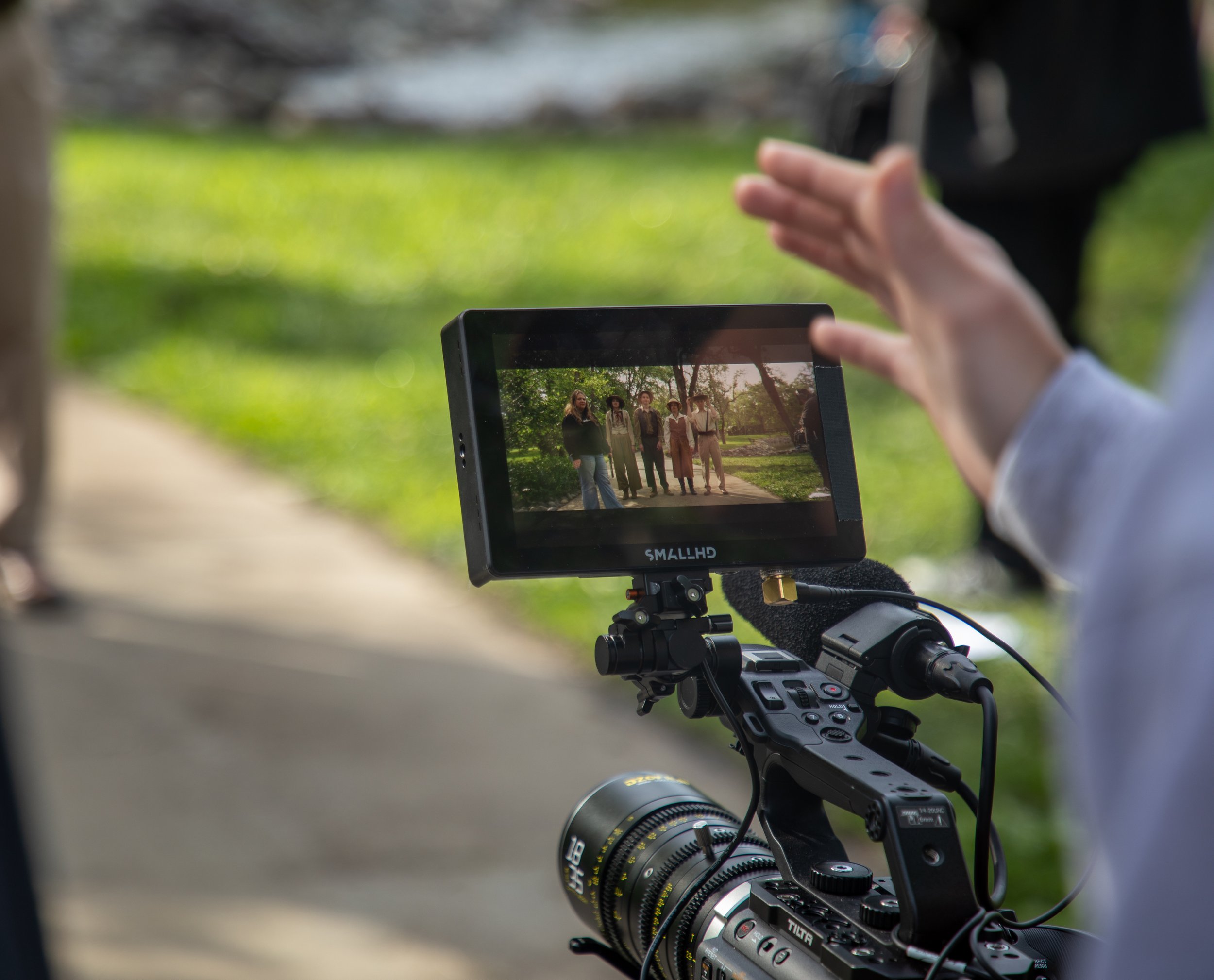Close-up of a filmmaking monitor mounted on a camera rig, showing a scene with five people in safari clothing outdoors.