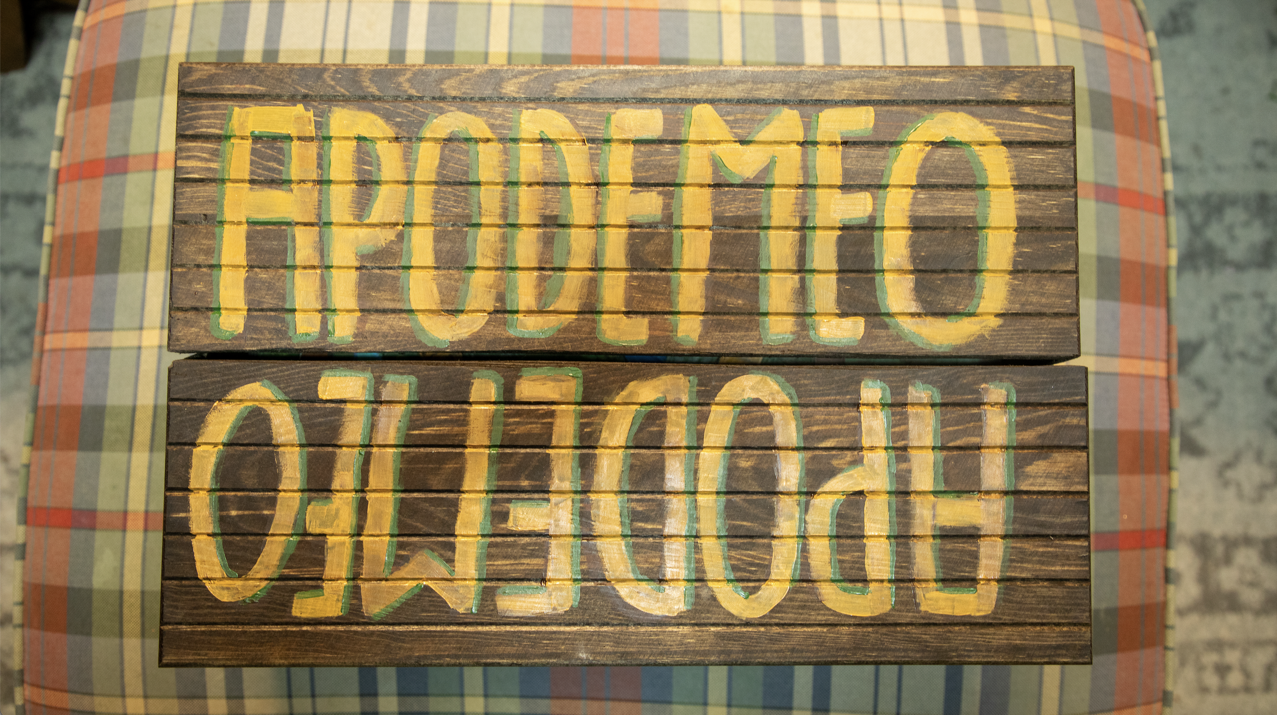Wooden sign with painted yellow and green letters spelling "APODEMEO" on a table with a checkered tablecloth.