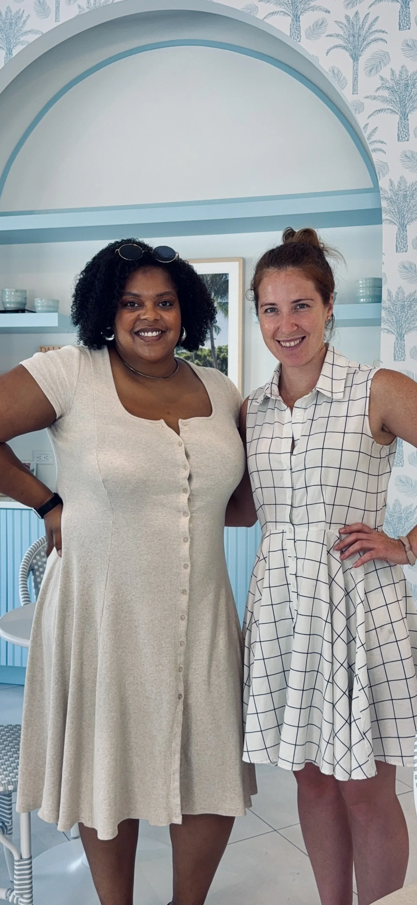 Brittani Millington and Sophie DeWaal standing together in front of the blue arched alcove at Arya Tea Bar.