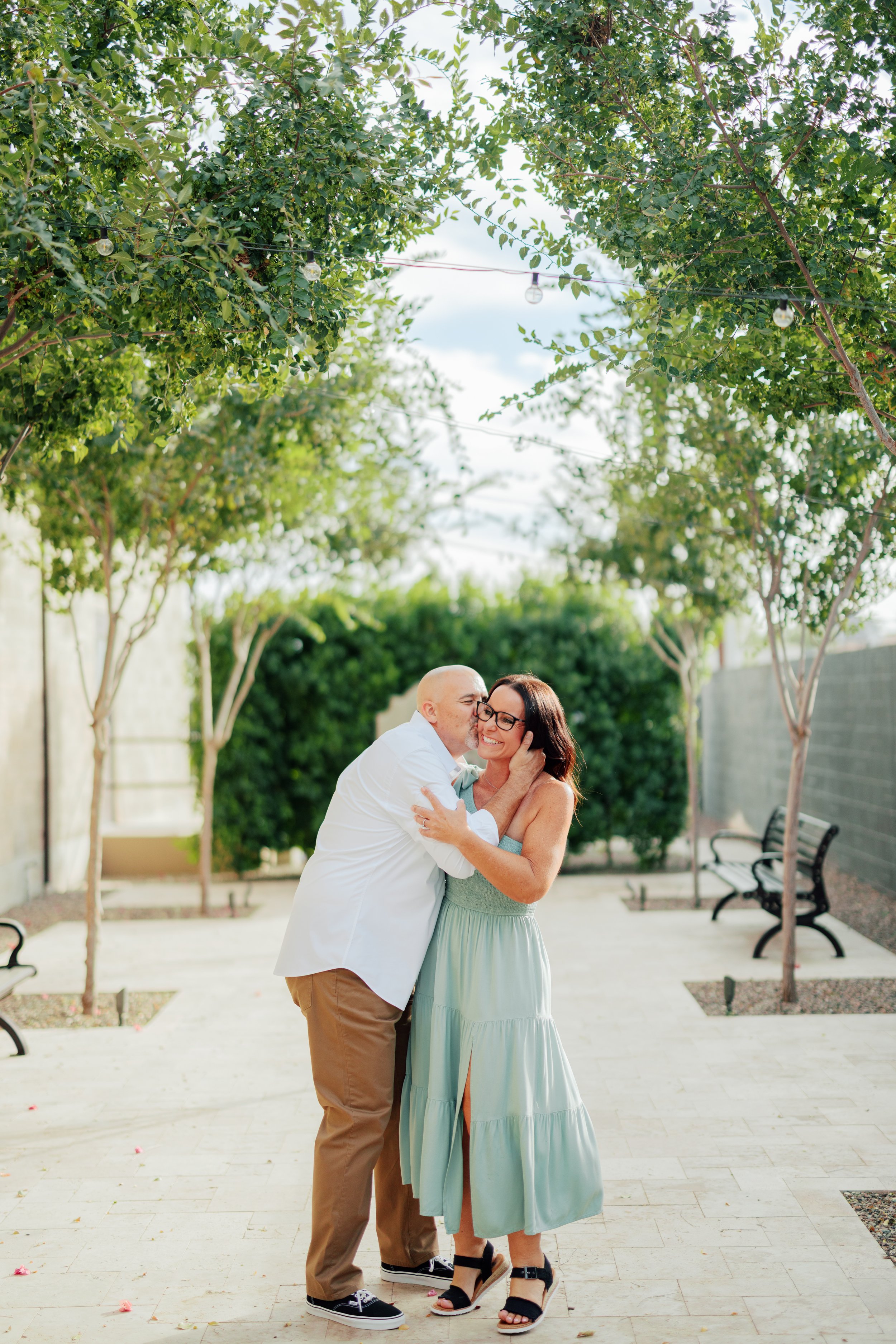 Engaged couple smiling and embracing during an outdoor engagement photography session in a park setting.