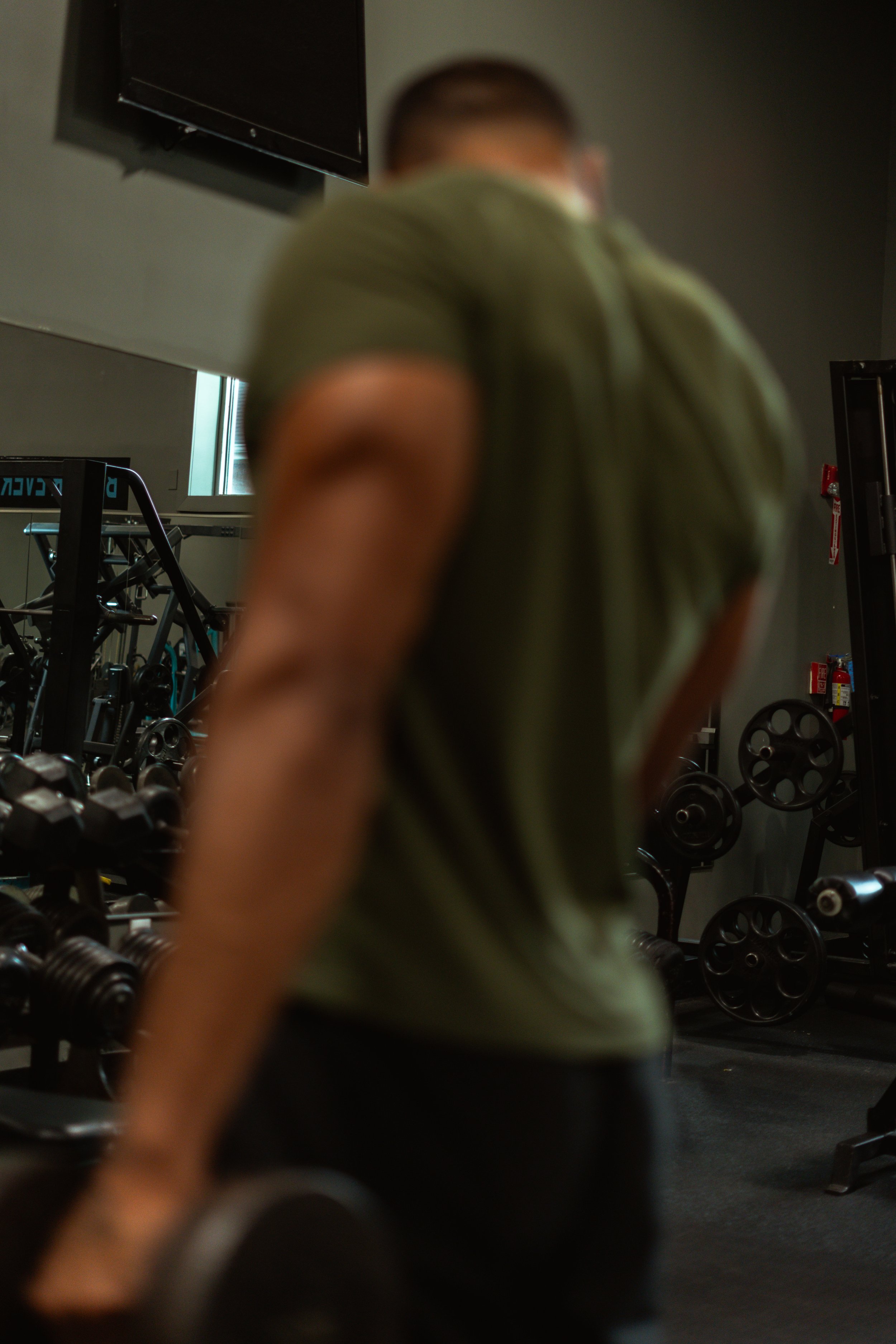 Blurred image of a person in a gym, with gym equipment like dumbbells and weight plates visible in the background.