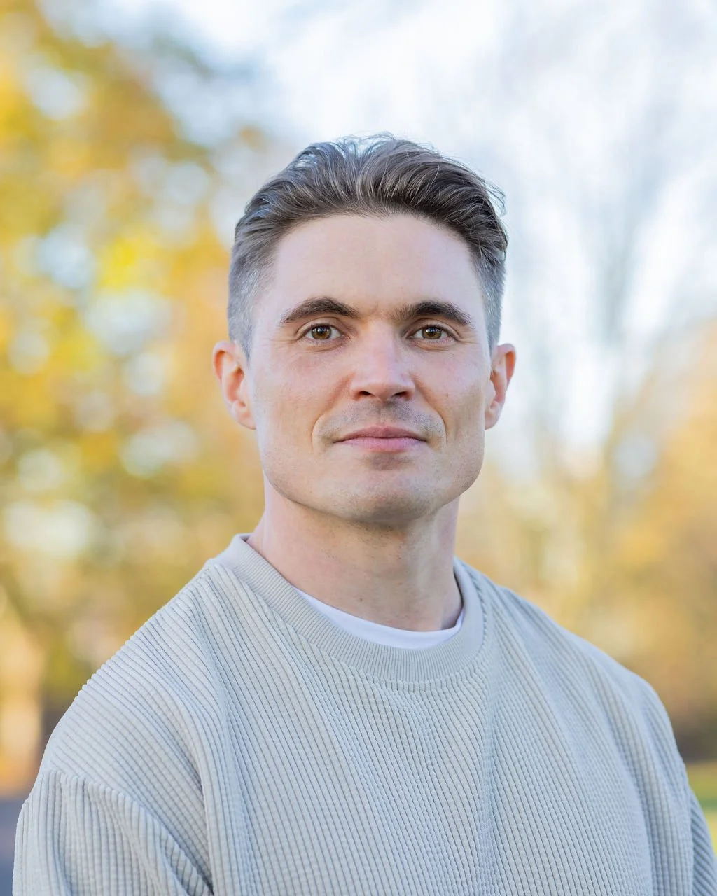 Portrait photo of man with dark blonde hair in cream-coloured top, looking at the camera smiling. Pictured: Owen Hughes