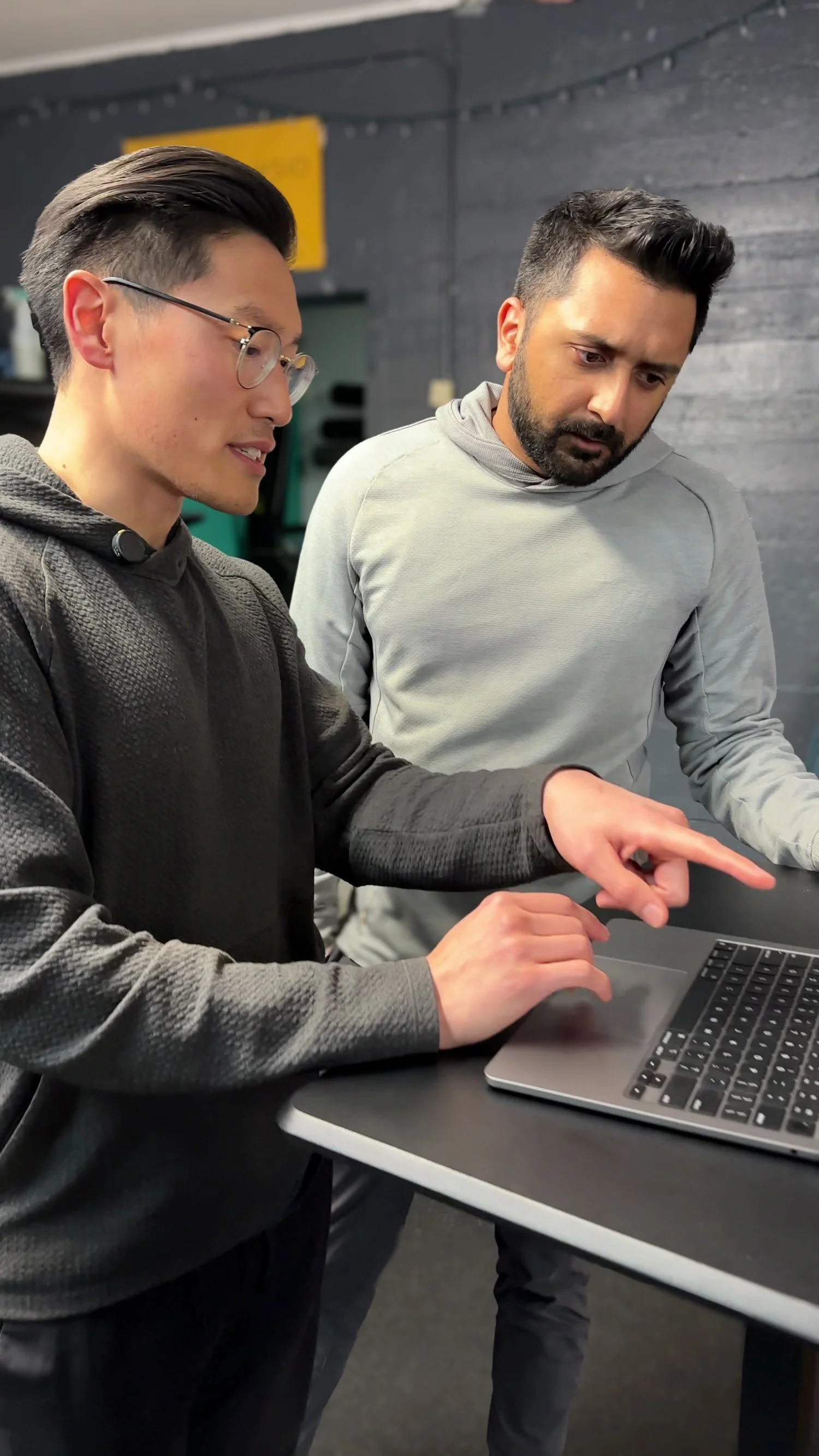 Two people collaborating at a laptop, one pointing at the screen, both wearing casual sweaters.