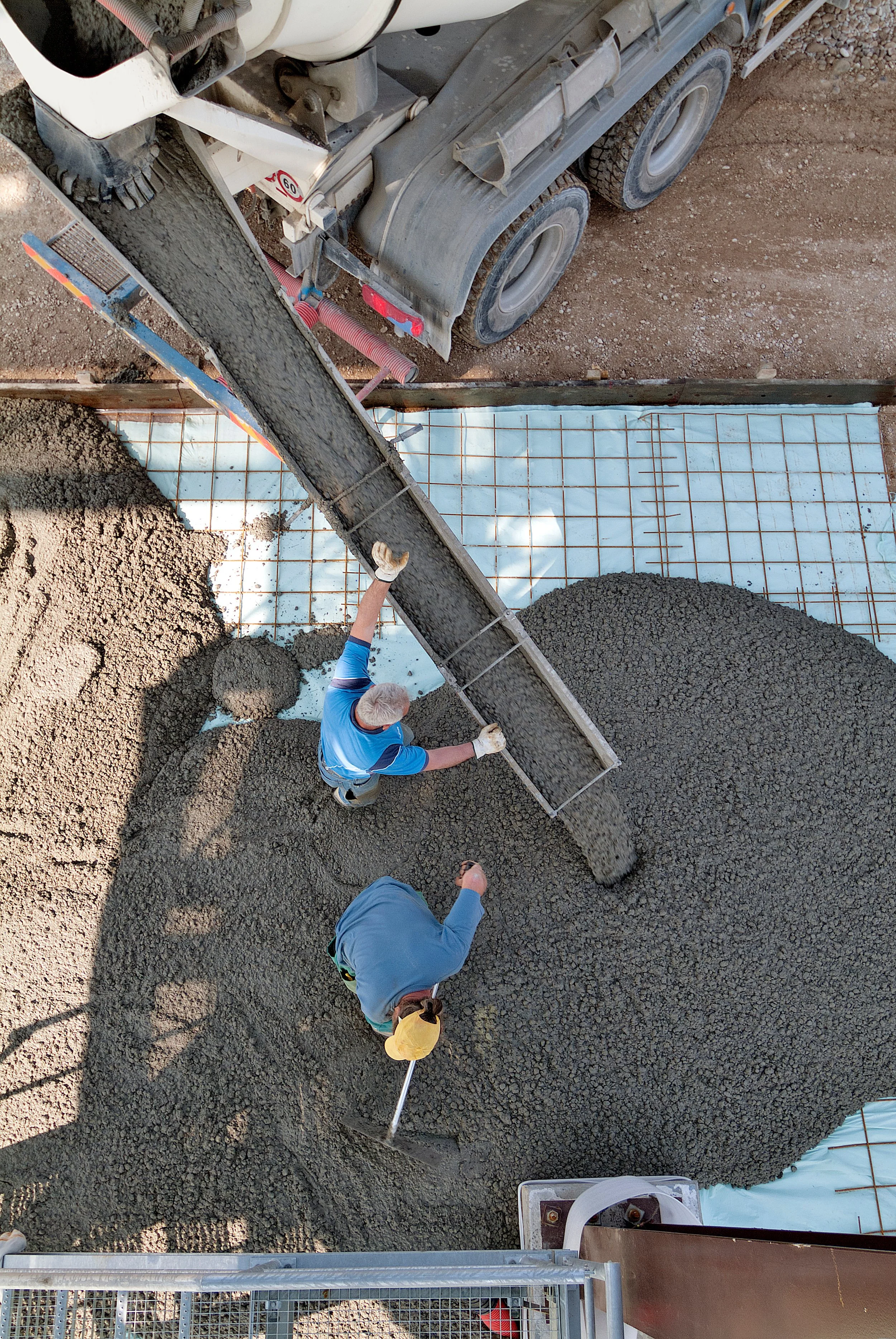 Construction workers pouring and leveling concrete on a building site, viewed from above.