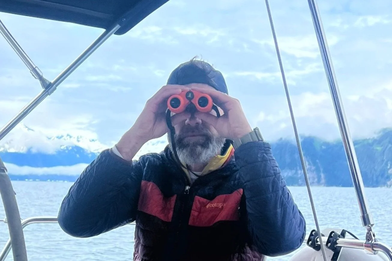Funny picture of a person on a sailboat looking at the camera with binoculars with ocean and mountains in the background - Resurrection Bay, Seward, Alaska. Sailaway Alaska, Seward Boat Tour