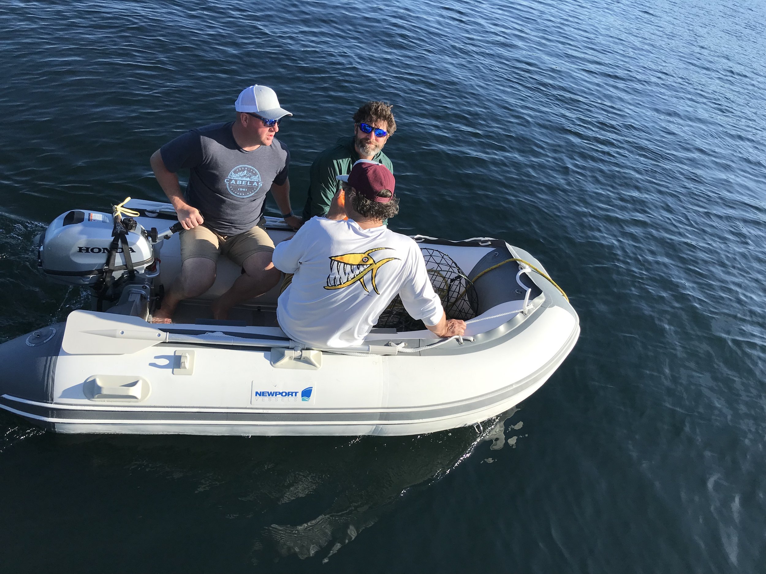 Three men in a small inflatable boat on a body of water.
