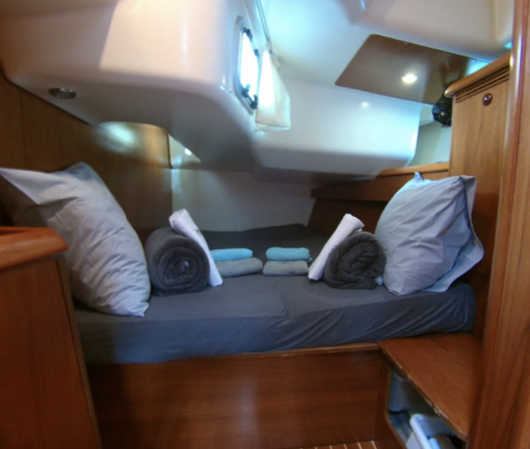Interior of a boat cabin with a made bed, pillows, and rolled towels.