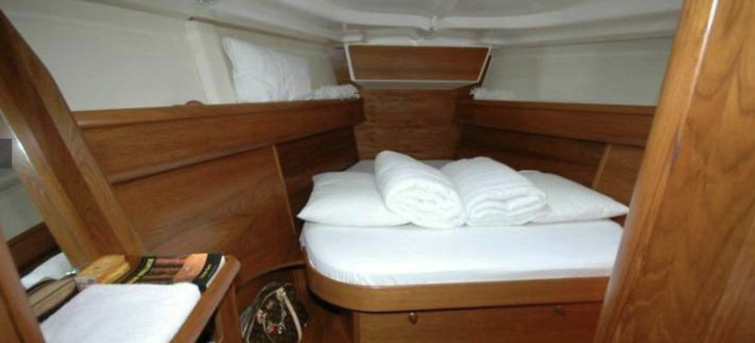 Small wooden cabin interior with bed, white linens, and books.