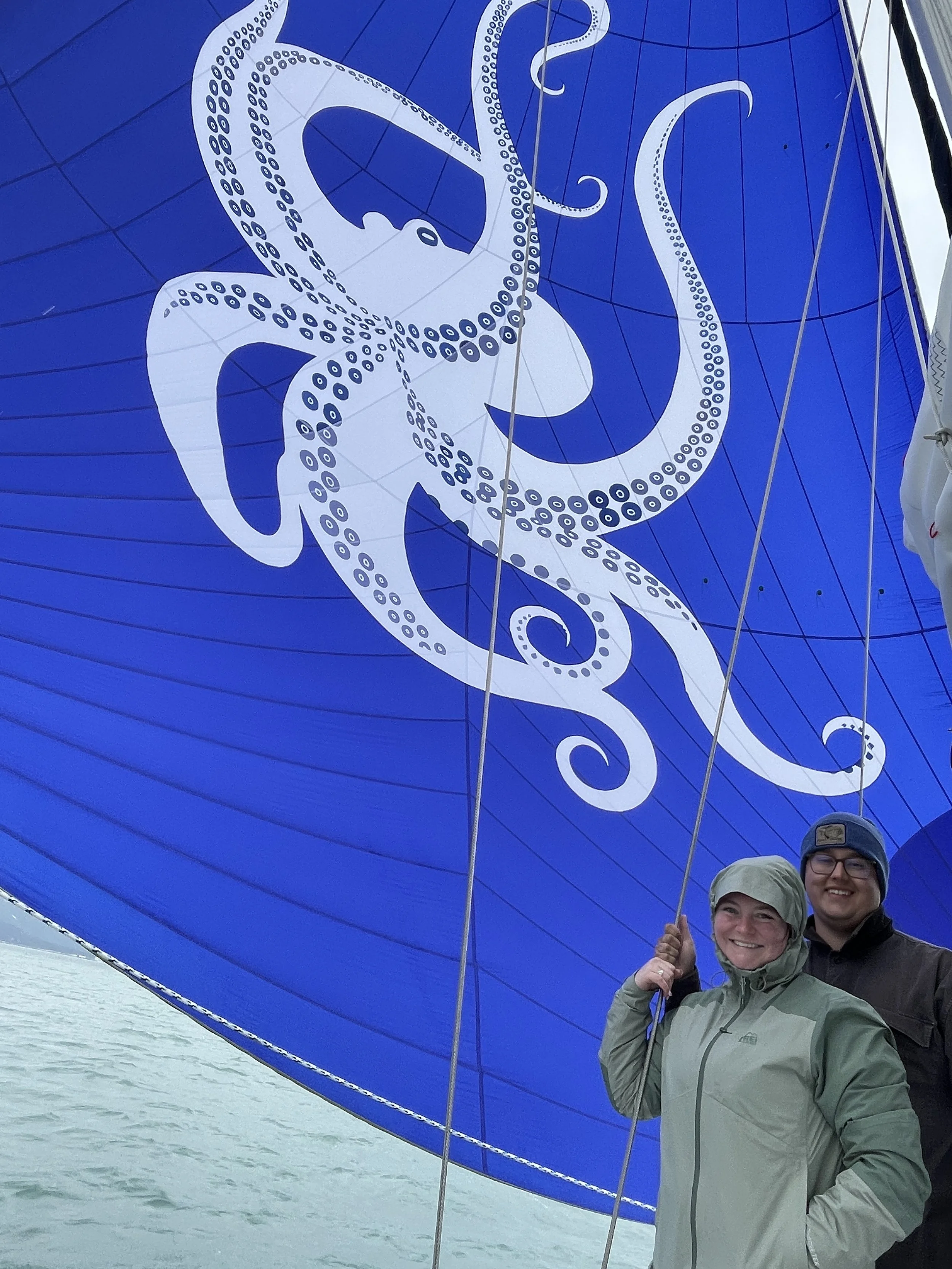 Couple standing with a custom, blue sail with a large white octopus printed on it. Sailaway Alaska, Seward Boat Tour
