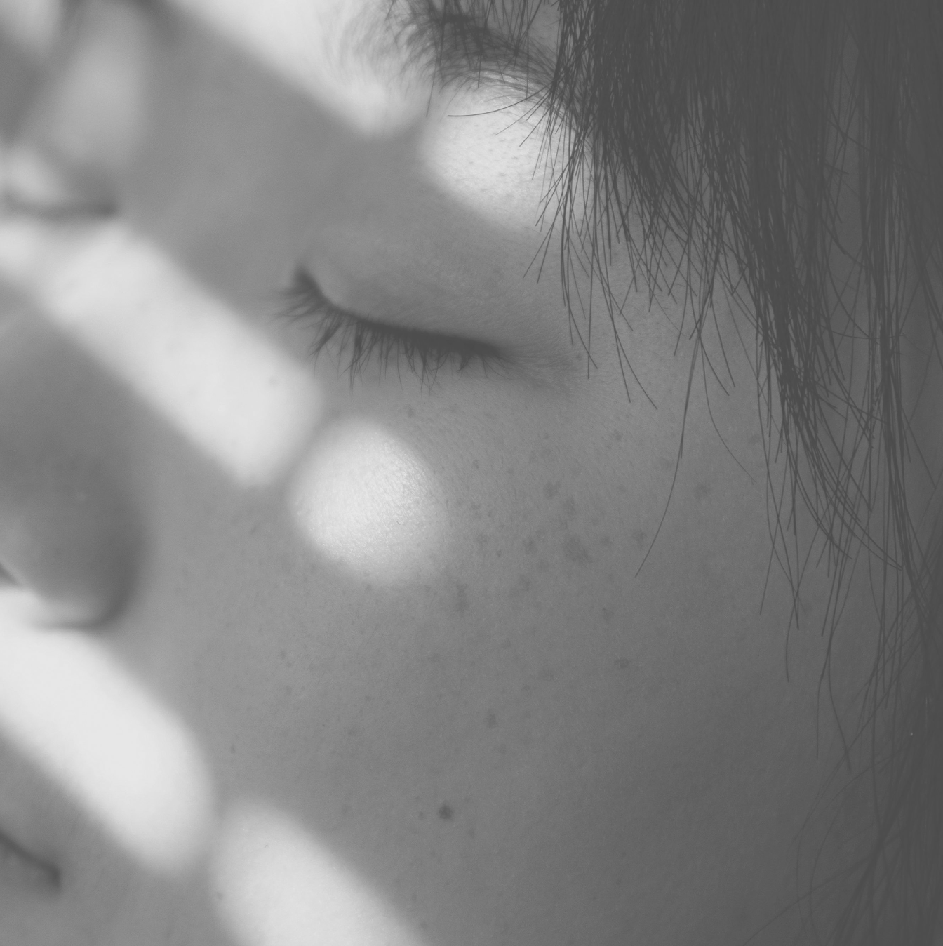 Close-up of a person's face with closed eyes and shadows.
