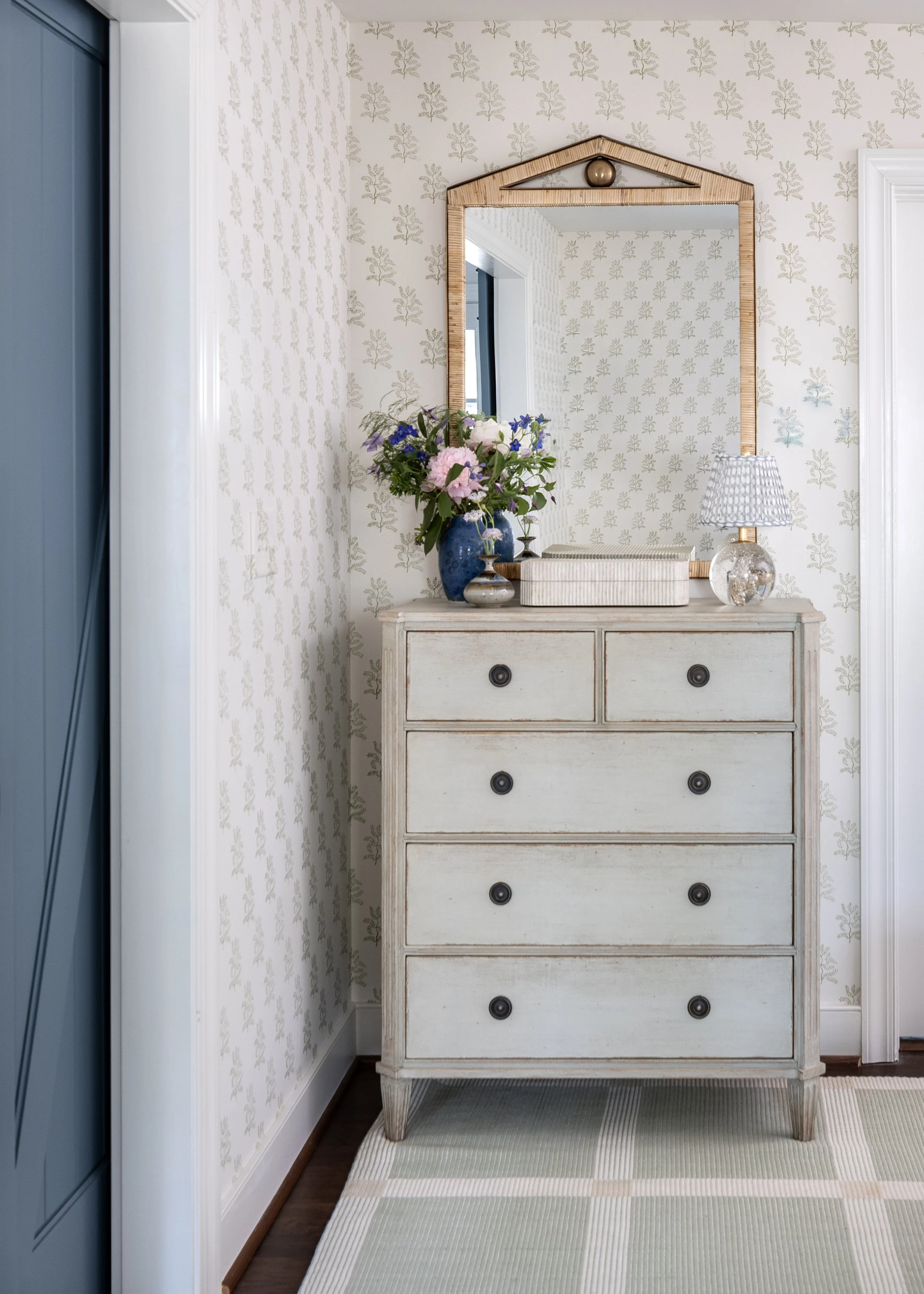 Detail of guest bedroom with a painted dresser featuring patterned wallpaper, classic lighting, and layered decorative styling