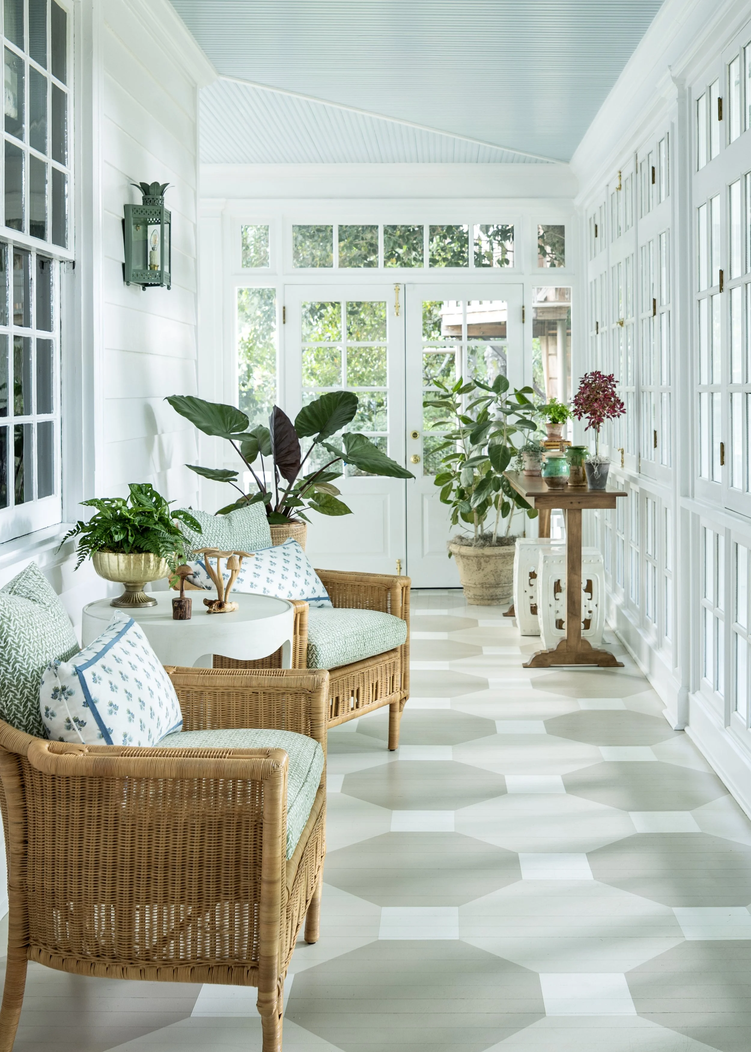 Sunroom featuring woven seating, house plants, custom painted floor, and expansive windows overlooking the landscape.