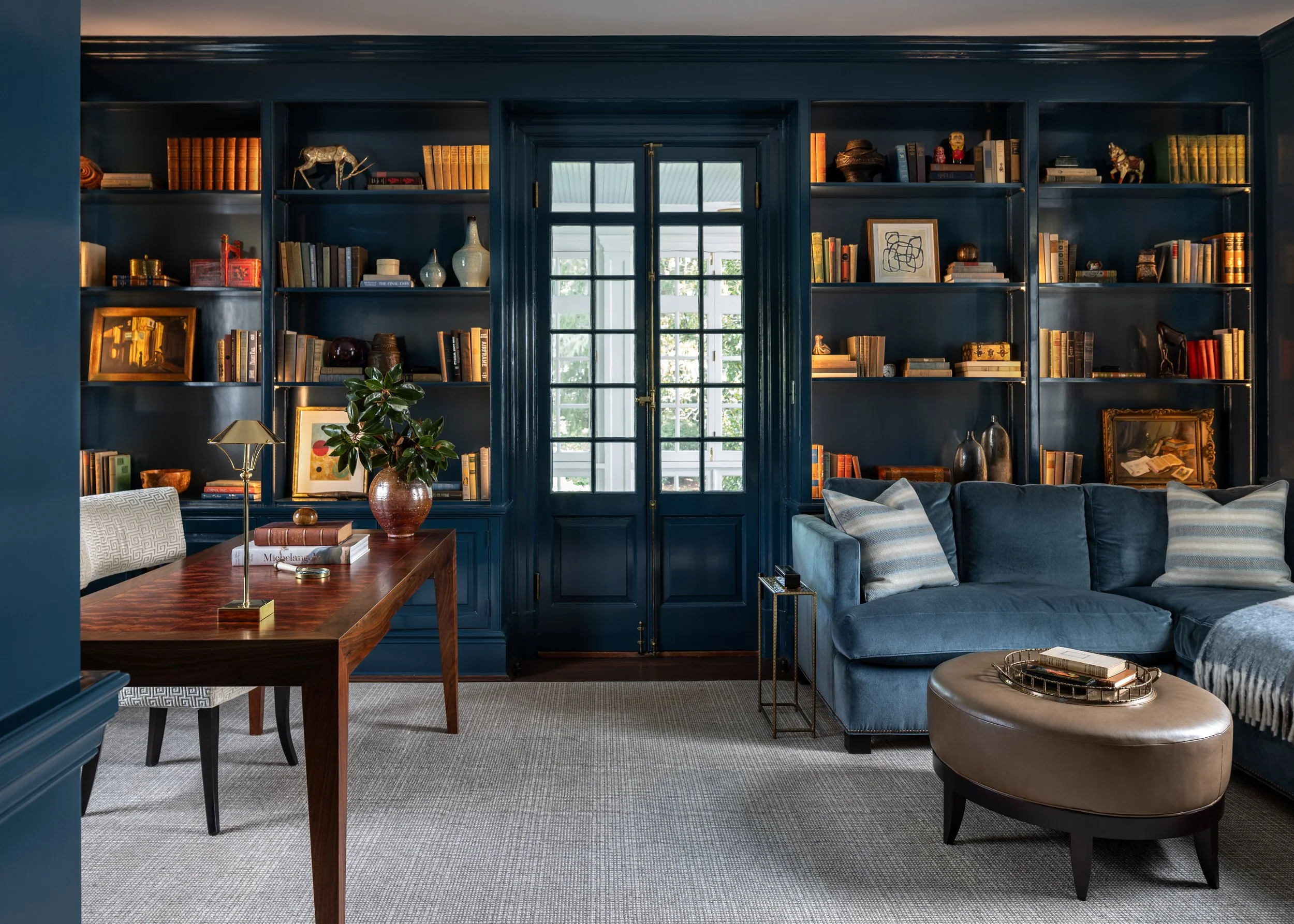 Home office featuring dark blue built-in bookcases, custom millwork, layered lighting, and collected furnishings.