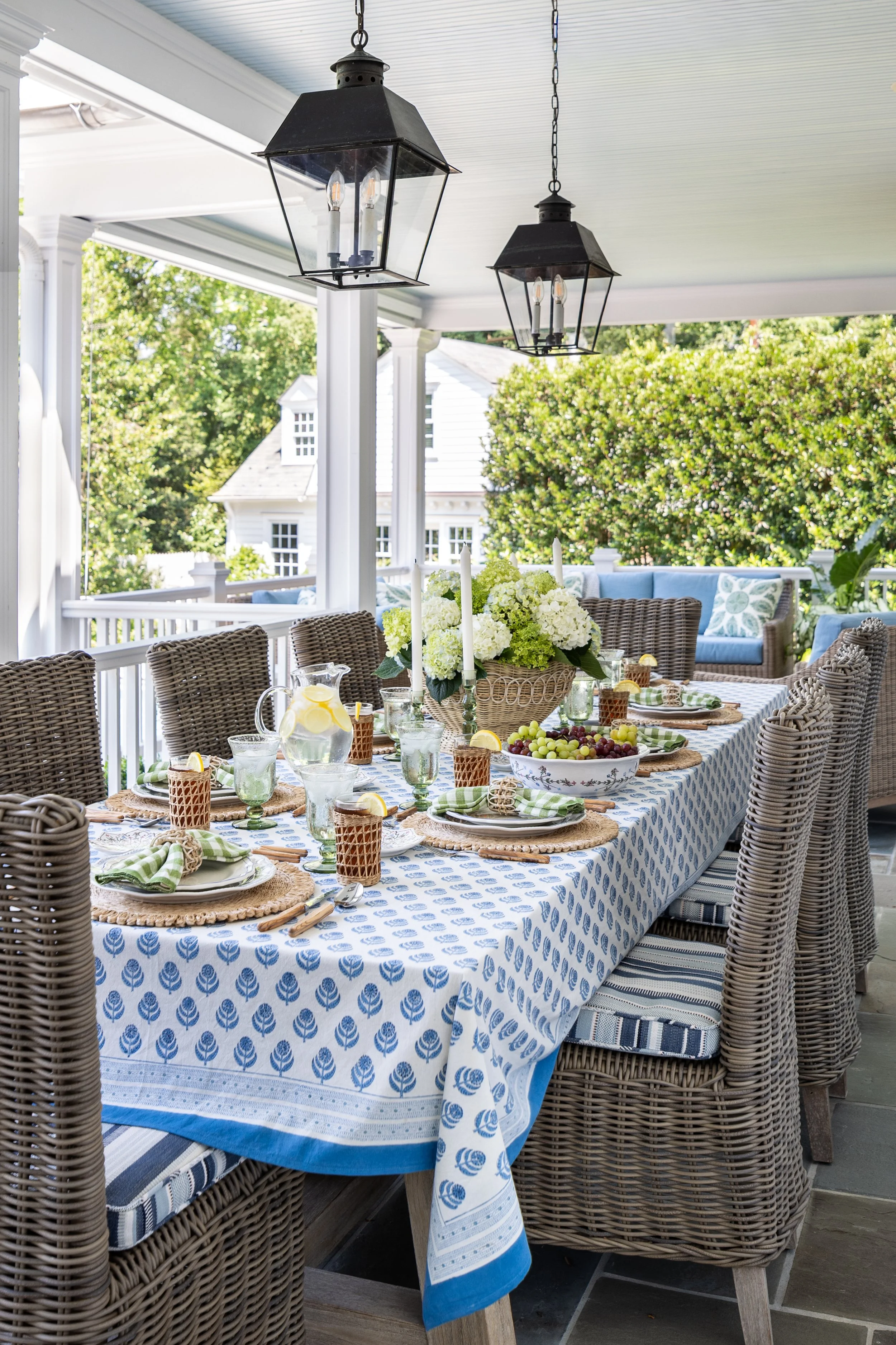 Covered outdoor dining space featuring wicker seating, layered table styling, and garden views.