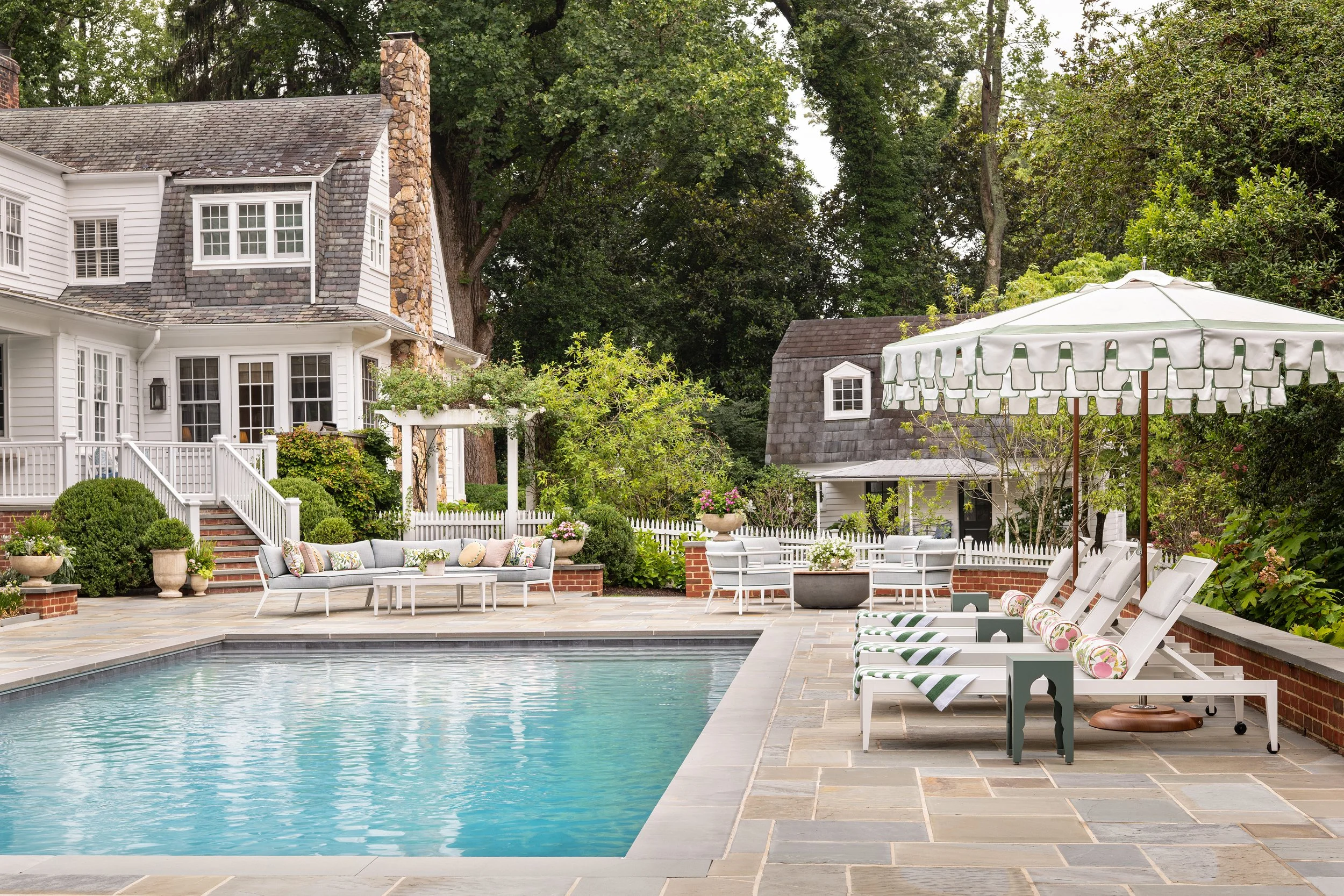 Inviting pool with traditional home featuring chaises, umbrellas and lounge seating.