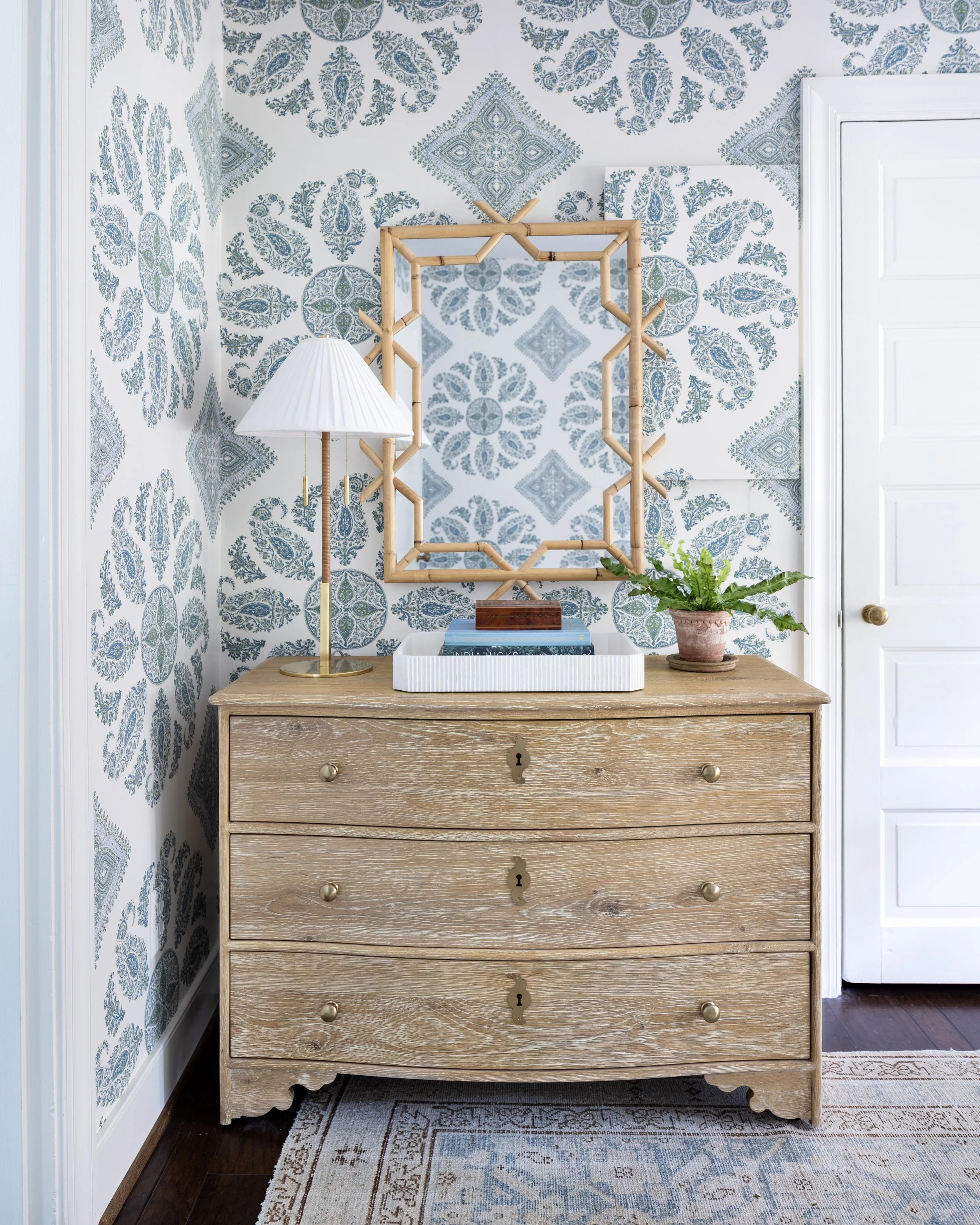 Wood dresser beneath a statement mirror with patterned wallpaper and classic styling.