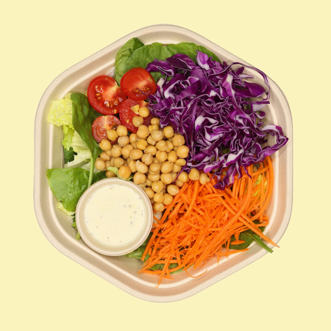 Mixed salad with shredded carrots, purple cabbage, cherry tomatoes, chickpeas, lettuce, and a small container of creamy salad dressing