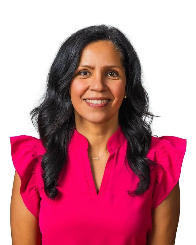 A woman with long black hair wearing a bright pink blouse, smiling against a plain white background.