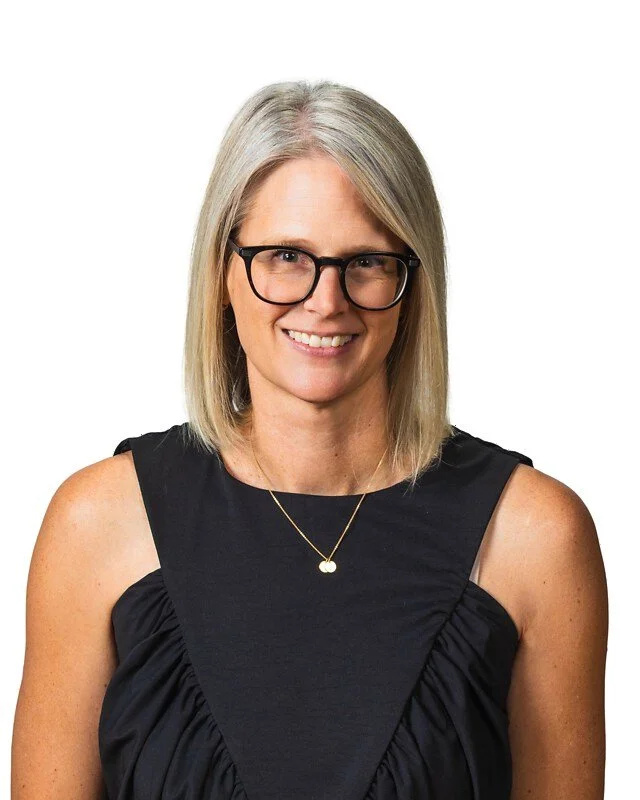 A woman with blonde hair, wearing glasses, a black sleeveless top, and a gold necklace, smiling at the camera.