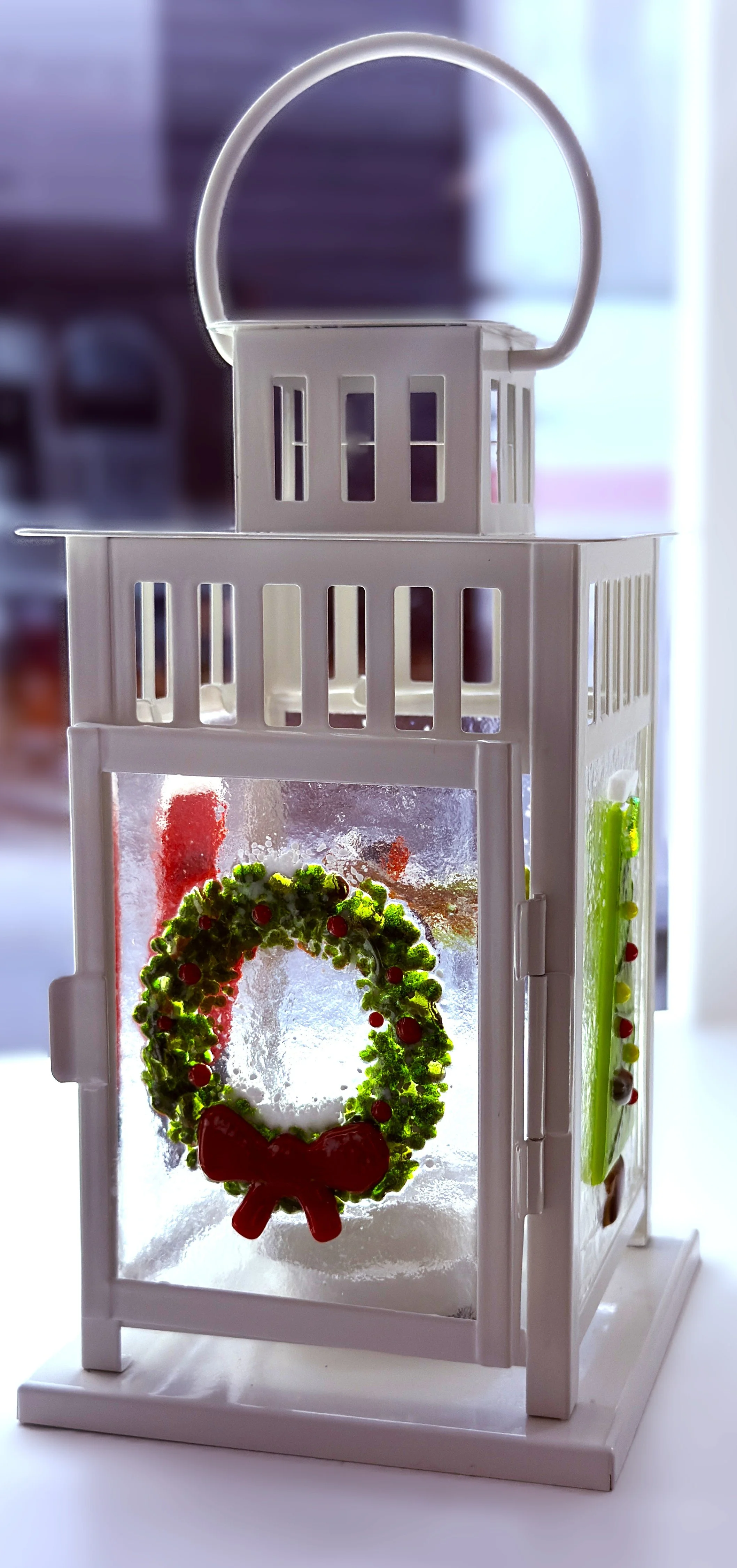 A cream coloured lantern with a glass Christmas wreath