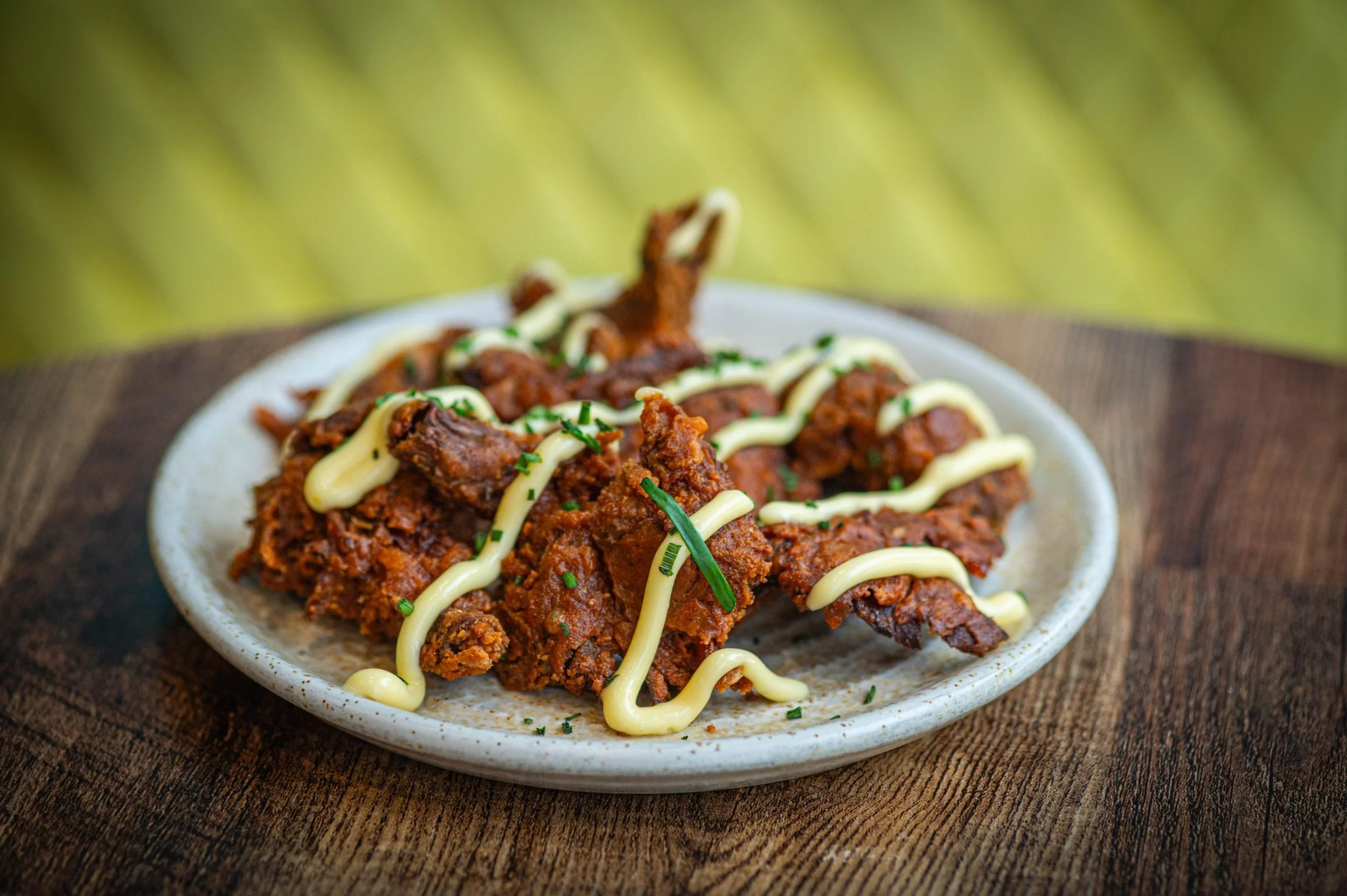 Plate of fried chicken drizzled with mayonnaise and chopped green herbs on a wooden table.