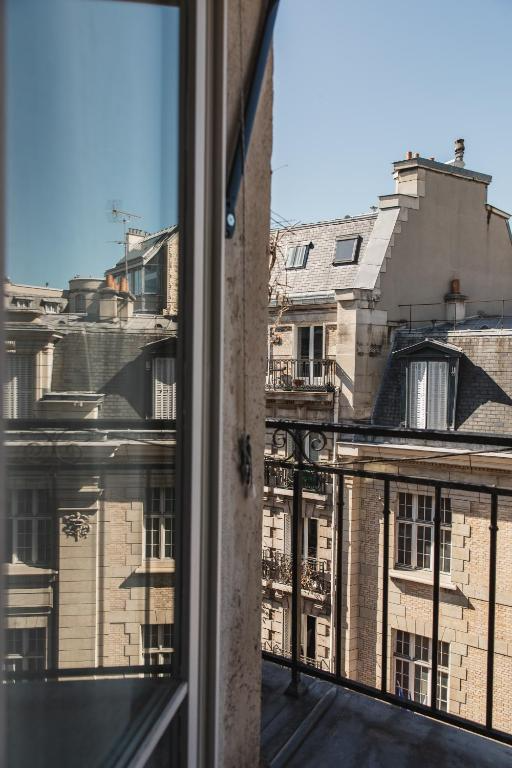 View from an apartment balcony showing neighboring Parisian buildings with classic architecture and slate roofs under a clear blue sky.